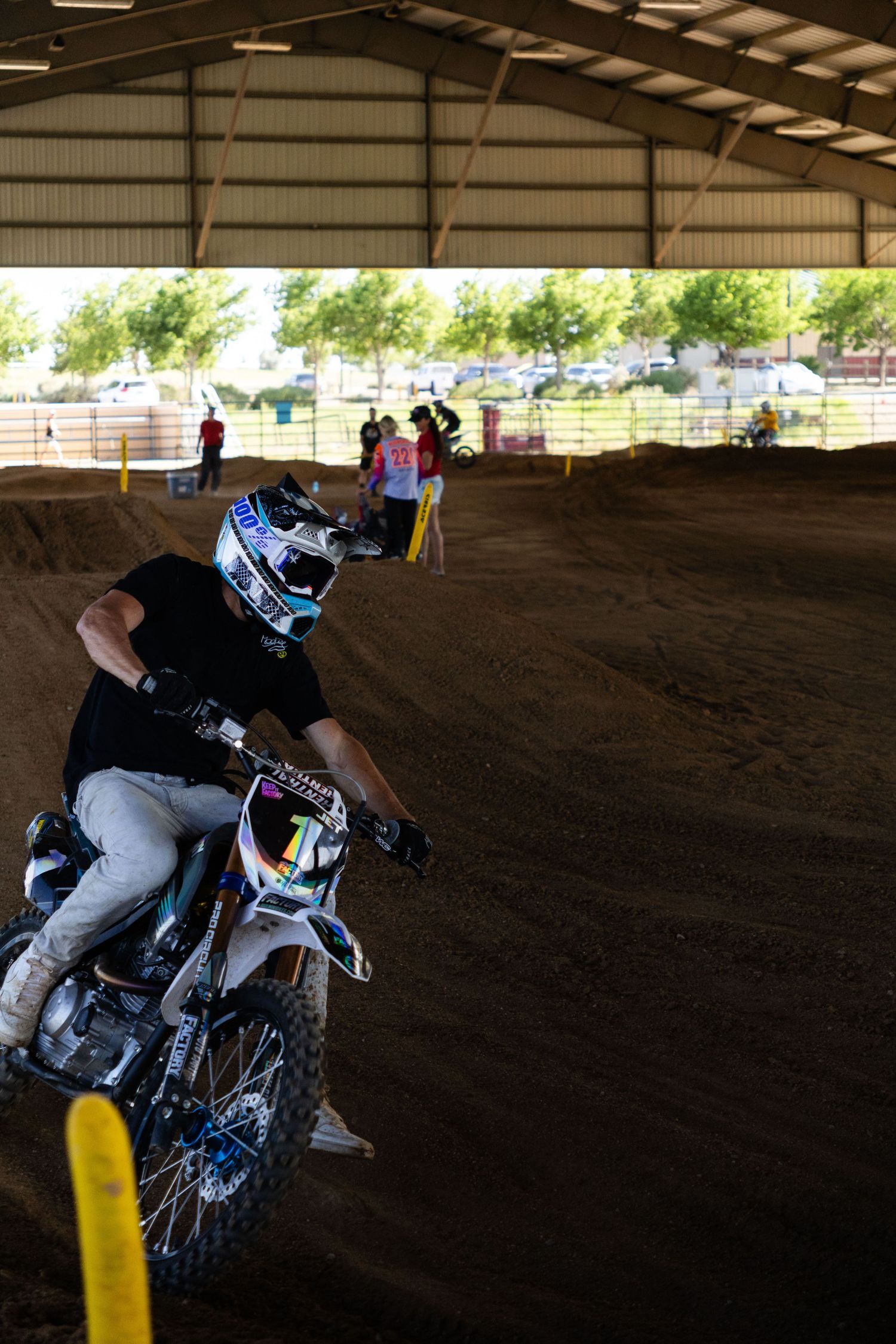 Motocross rider in black gear navigates bermed turn on indoor dirt track during supercross event.