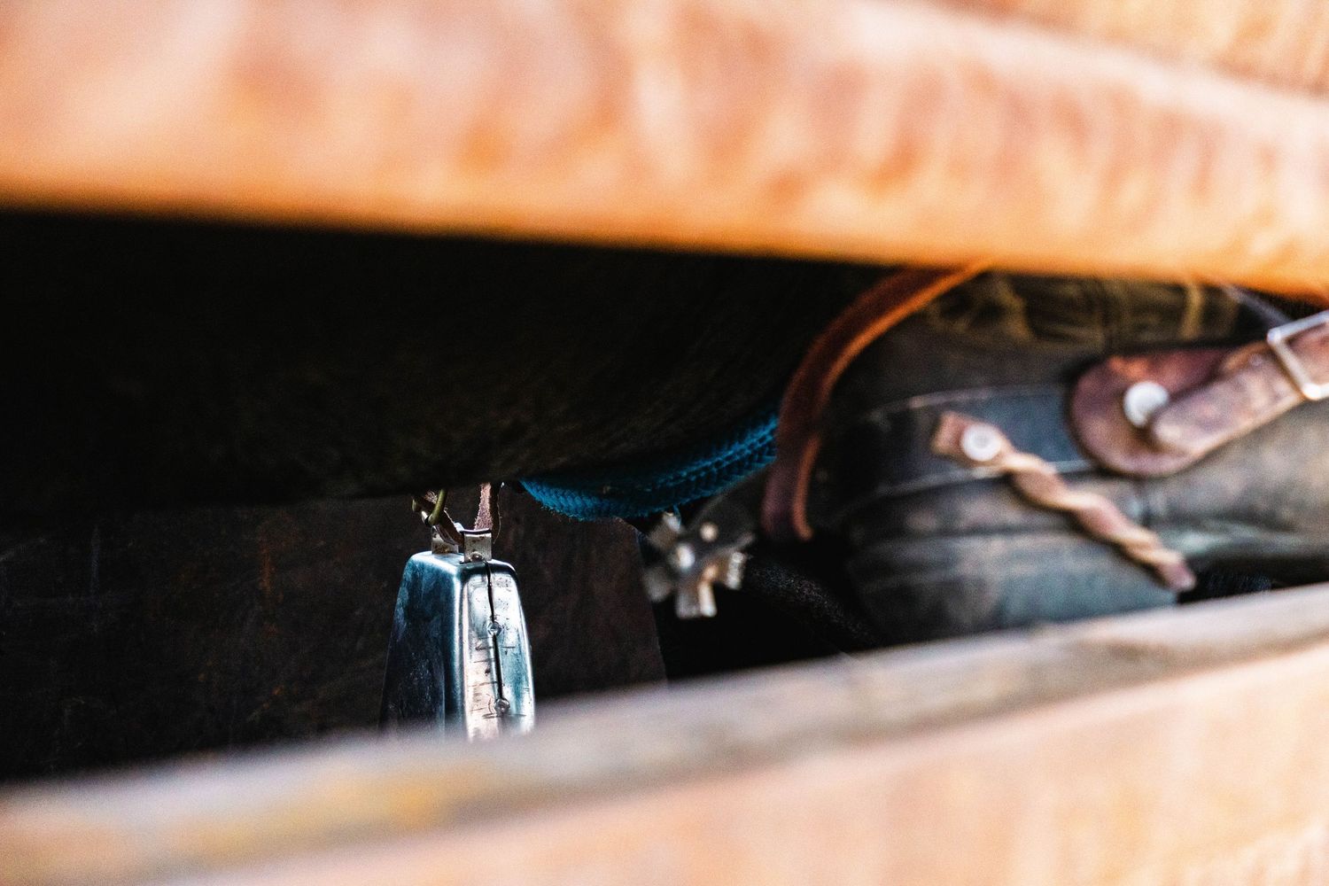 Close-up of leather horse tack, blue rope, and metal hardware stored in a rustic wooden box.