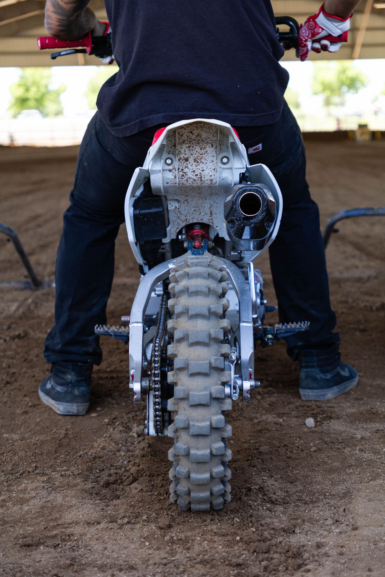 Close-up rear view of a muddy motocross dirt bike with knobby tire on sandy track.