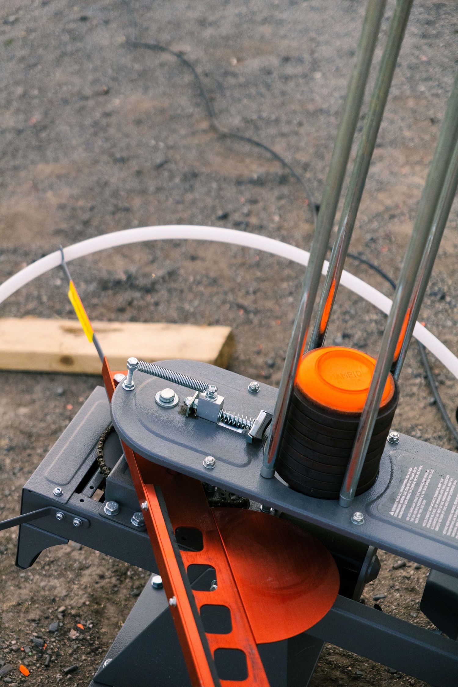 Close-up of an orange and gray clay pigeon trap machine with metal rods and spring mechanism outdoors.