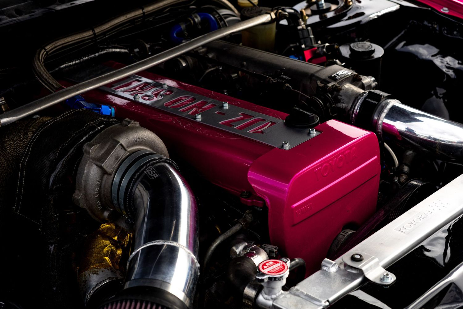 Close-up of a pink turbocharged engine bay with performance intake and custom valve cover.