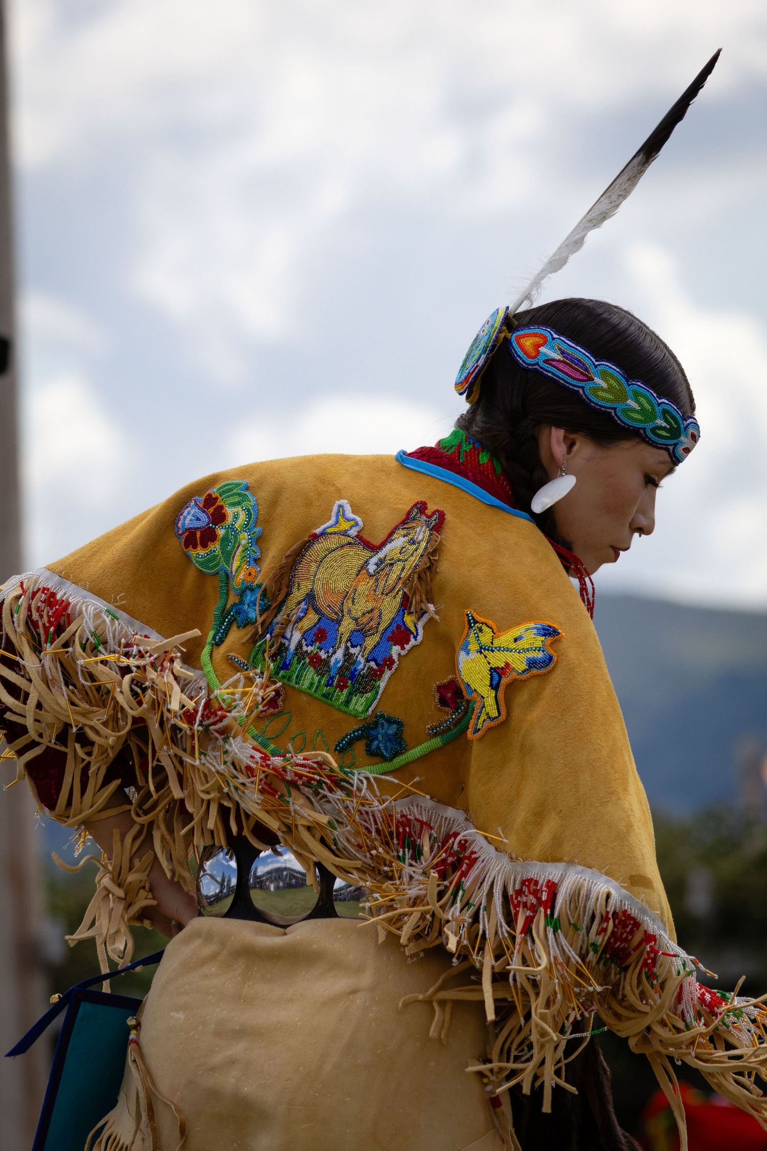Native American dancer in fringed buckskin regalia with wolf beadwork and bells at an outdoor powwow.