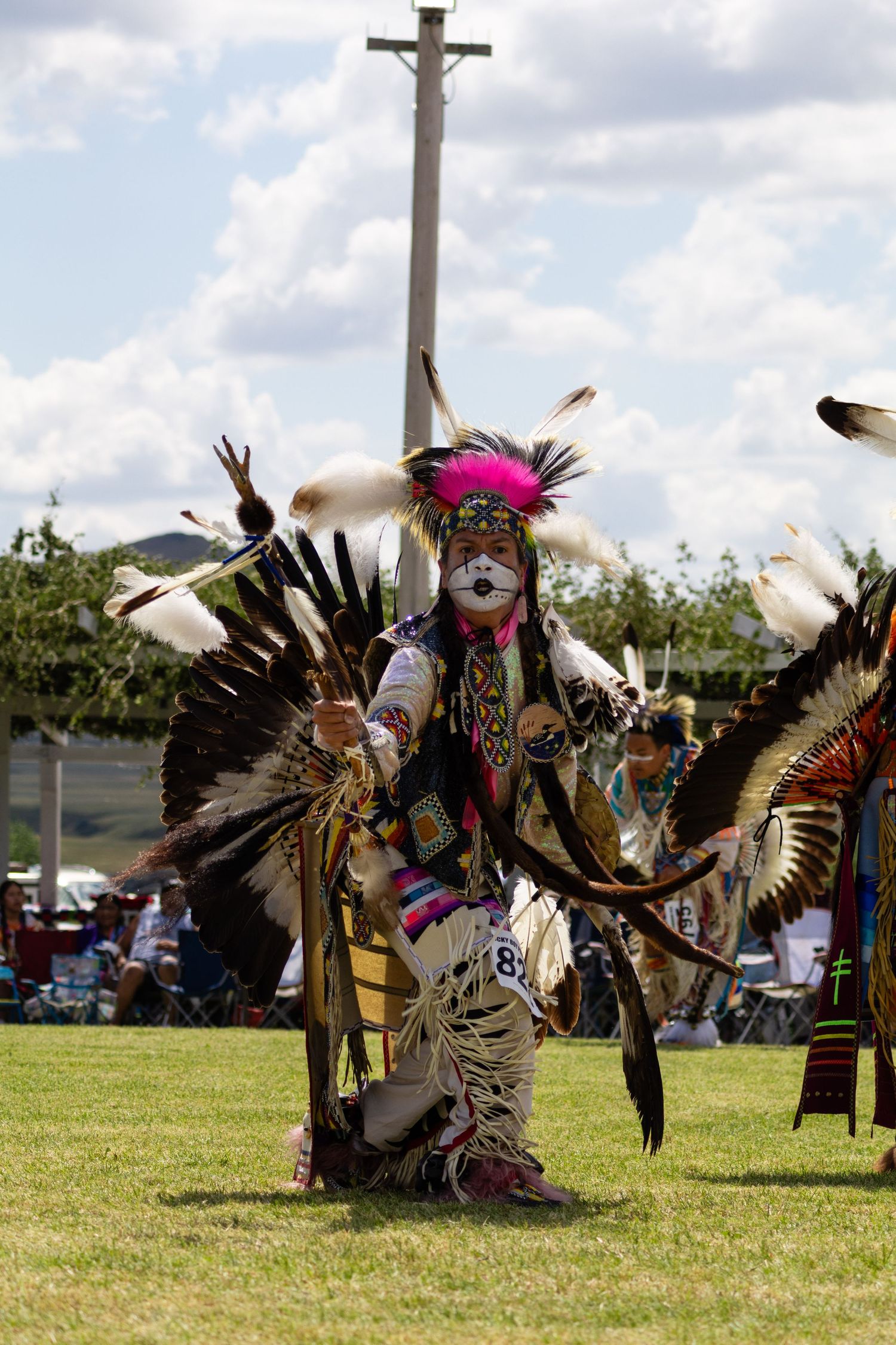 Native American dancer in colorful traditional regalia with large feathered wings performing at a powwow.