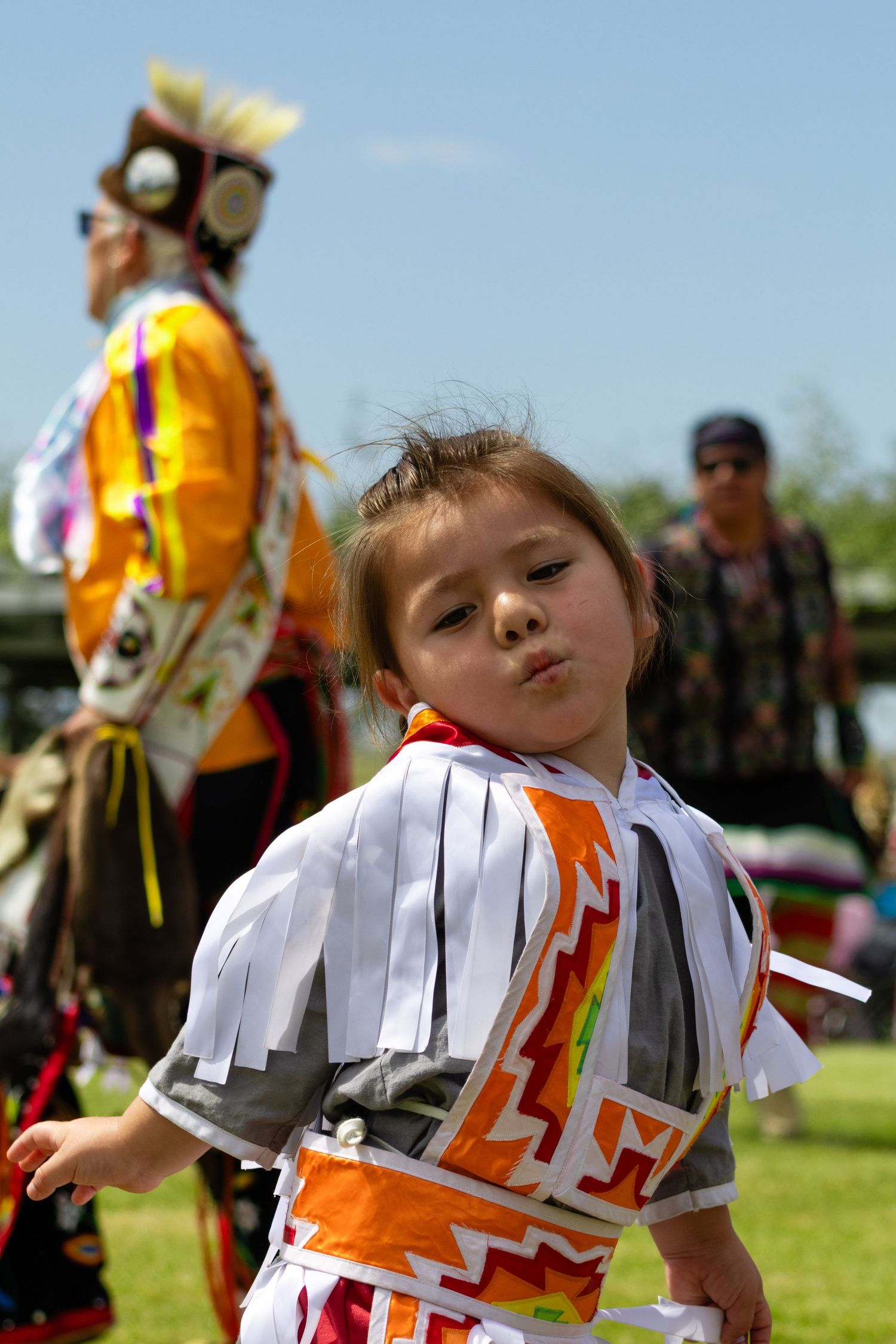 Young Native American girl dancing in traditional regalia at an outdoor powwow event.