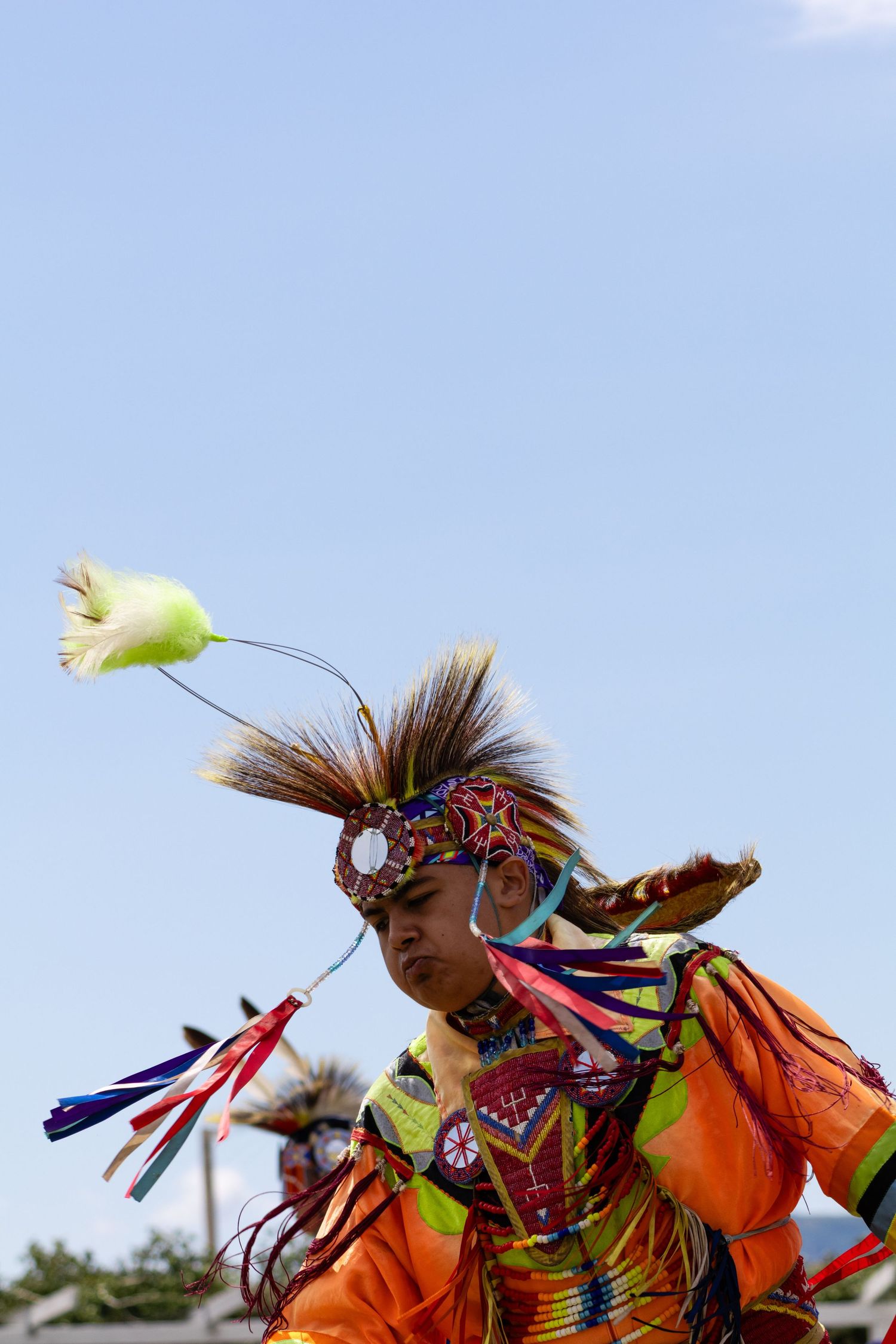 Native American fancy dancer in orange regalia with roach headdress performing at powwow.