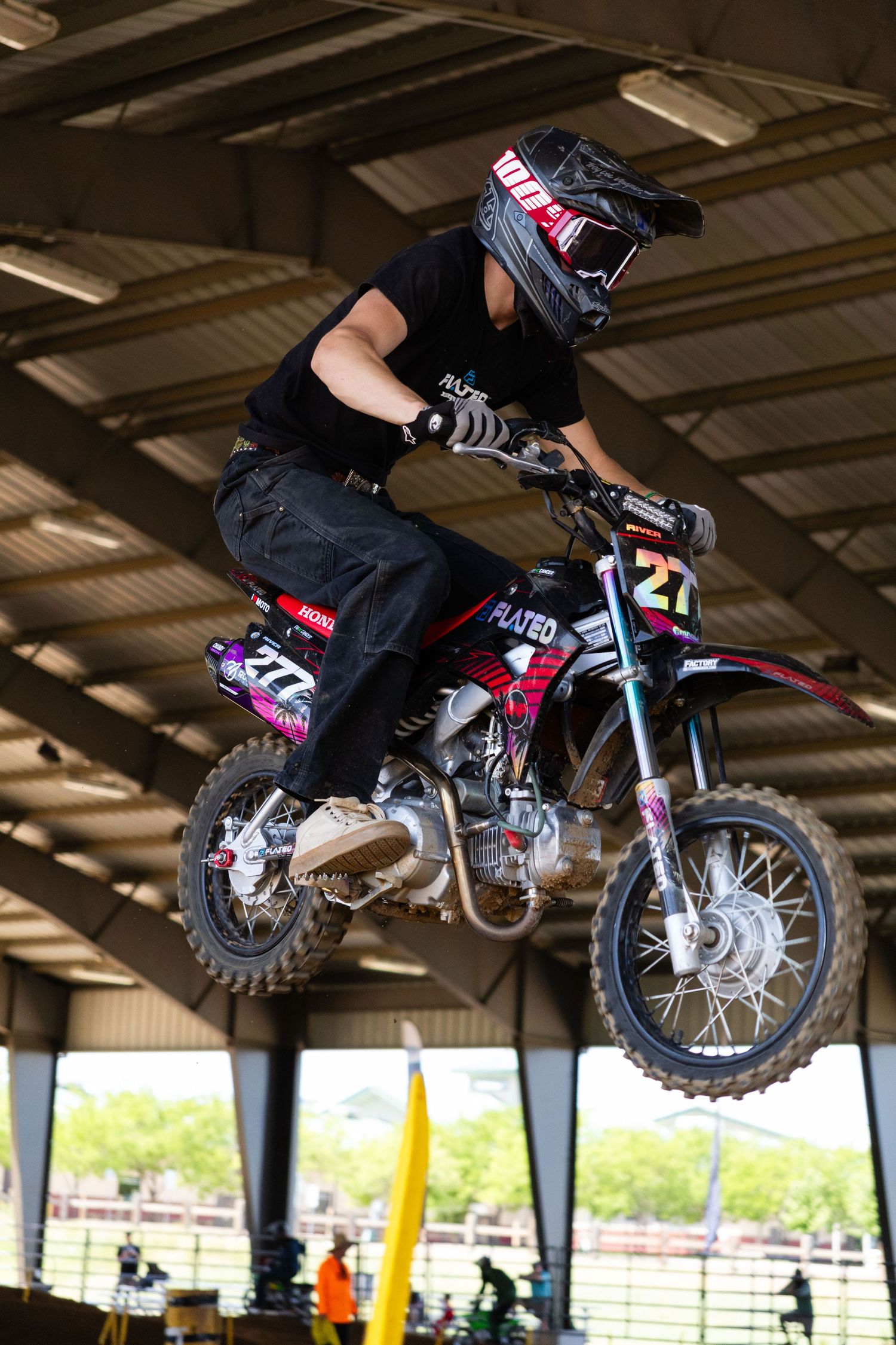 Close-up of motocross rider number 27 catching air on a dirt bike inside a covered supercross arena.