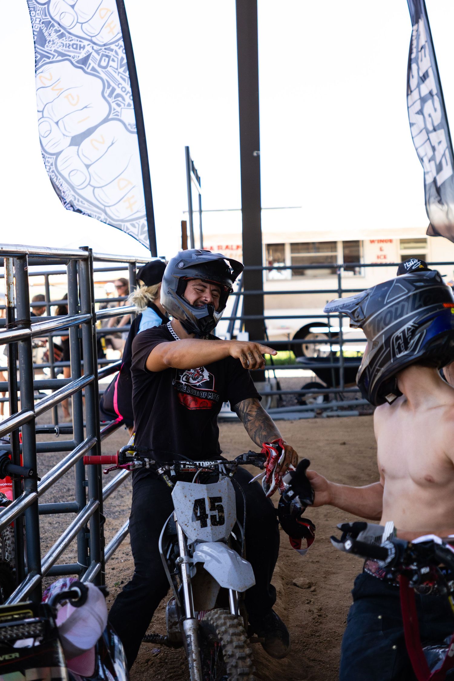 Two motocross riders in helmets fist bump near bike #45 at an indoor dirt arena event.