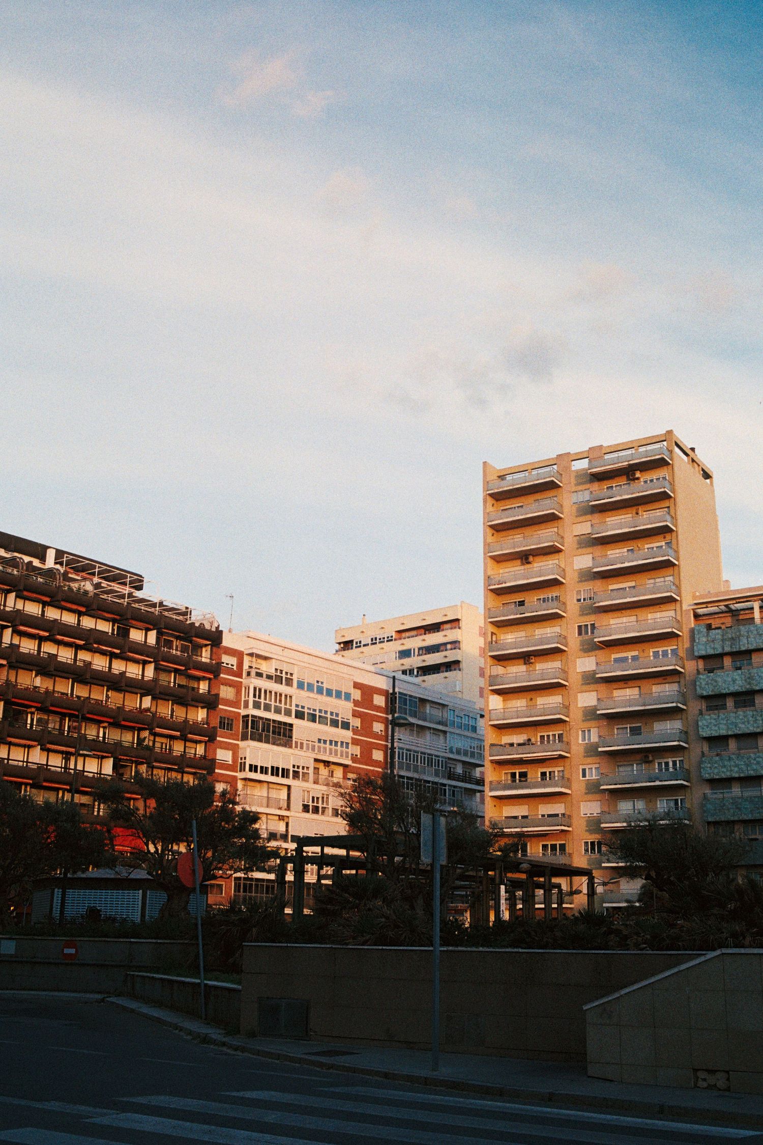 Urban apartment buildings bathed in warm golden sunset light against a blue sky with scattered clouds.