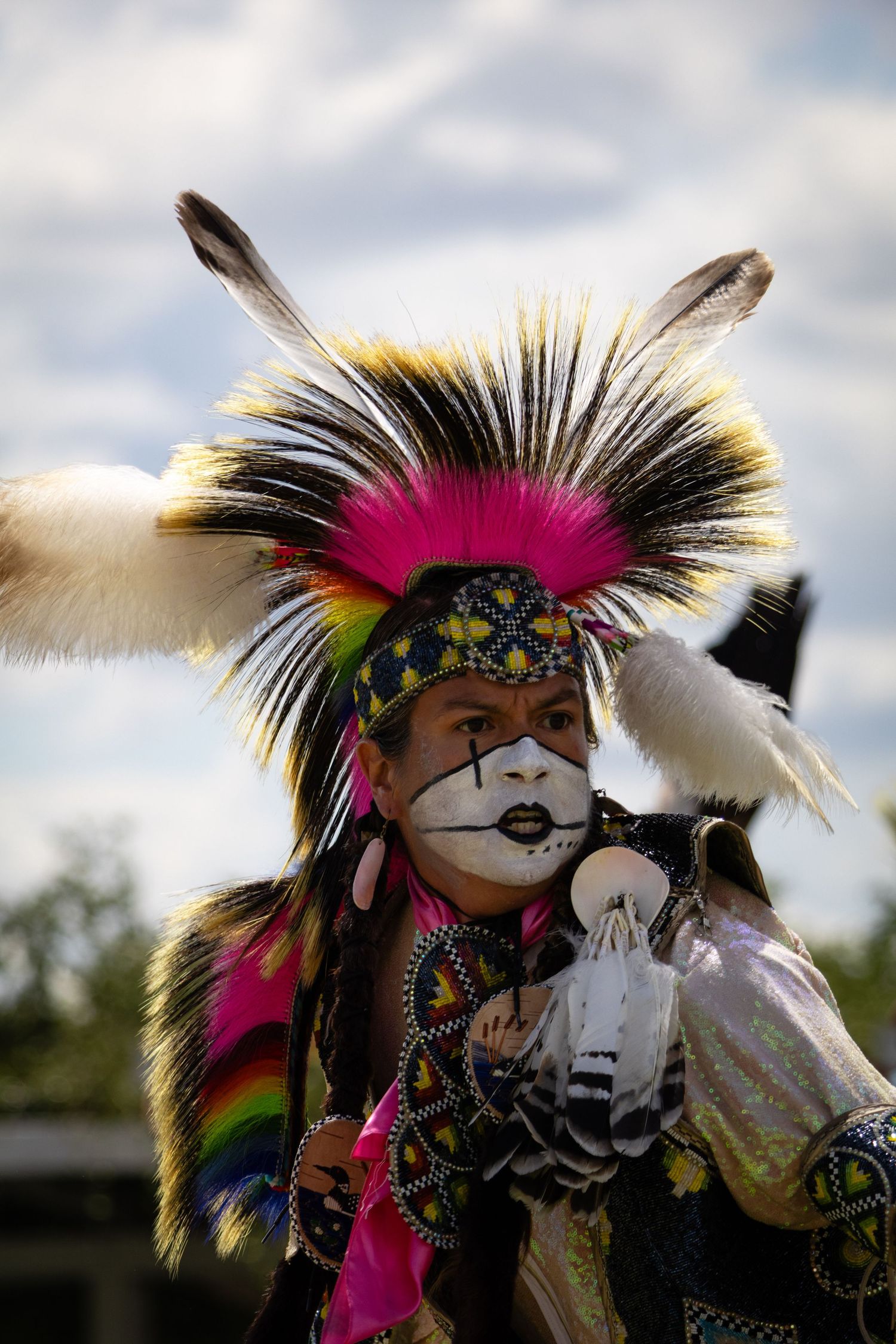 Close-up of Native American dancer with face paint and vibrant feathered headdress at a cultural powwow.