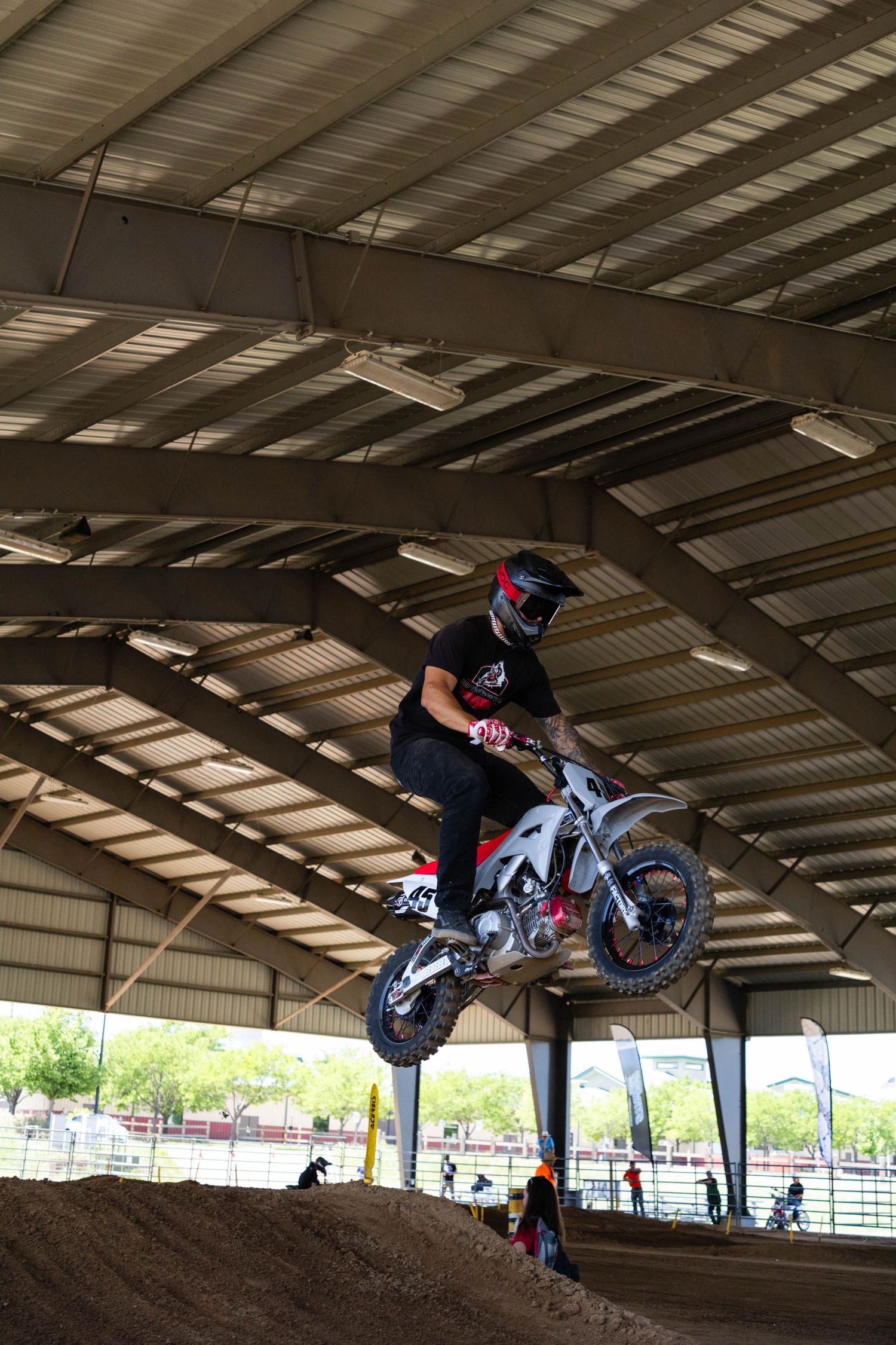 Motocross rider catching air on dirt bike jump inside large covered indoor motocross track.