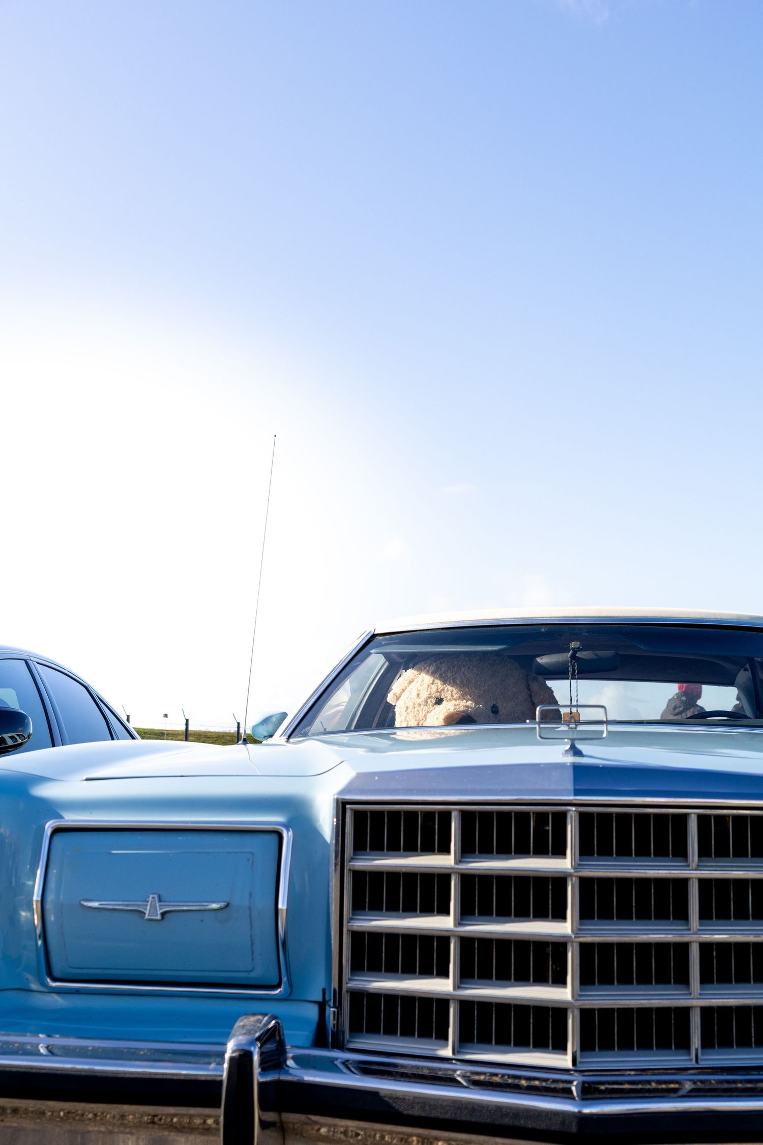 Vintage blue classic car with chrome grille and hood ornament parked under a clear blue sky.