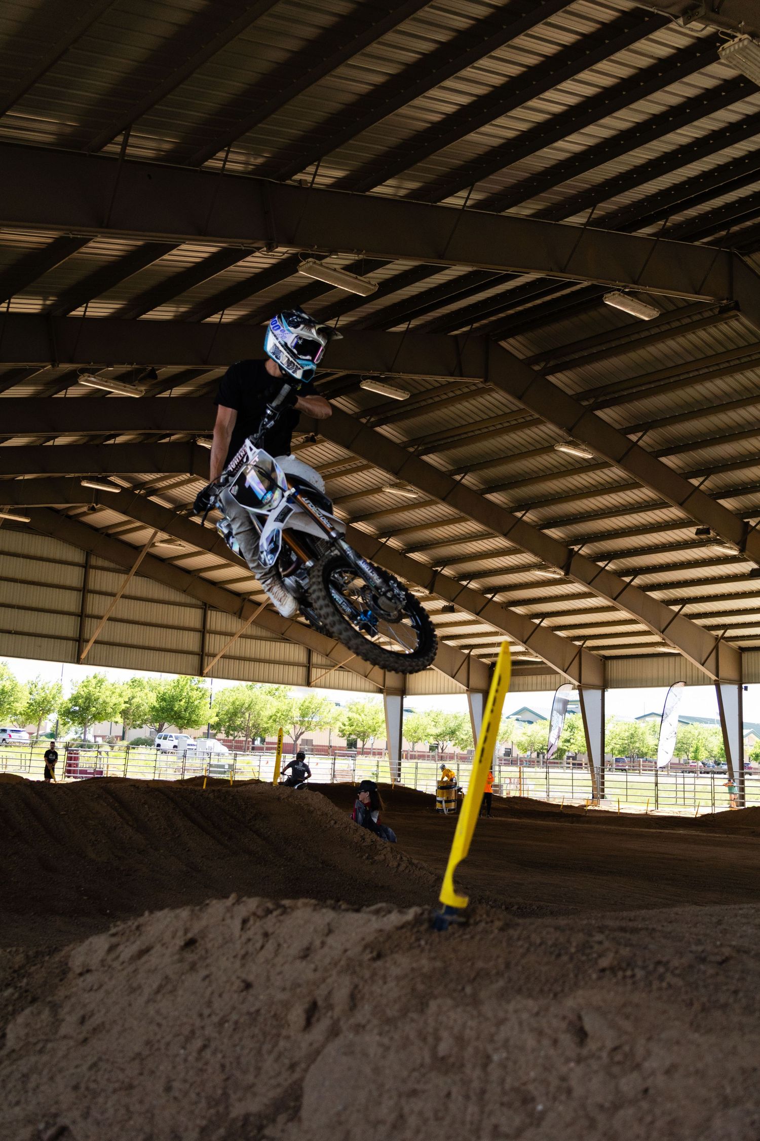 Motocross rider performs scrub jump over dirt mound at indoor supercross event.