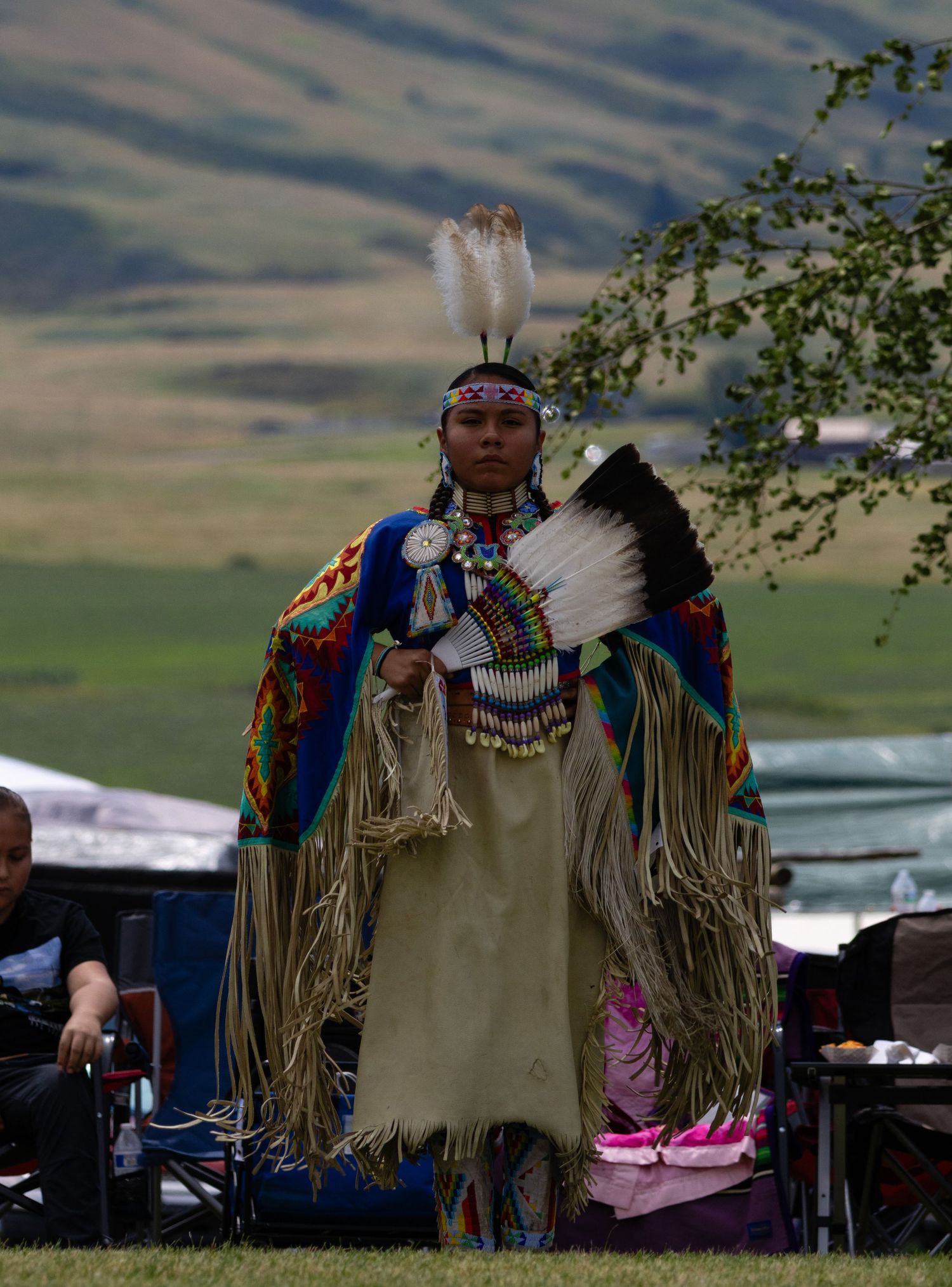 Native American woman in traditional fringed buckskin dress and feathered headdress at powwow.