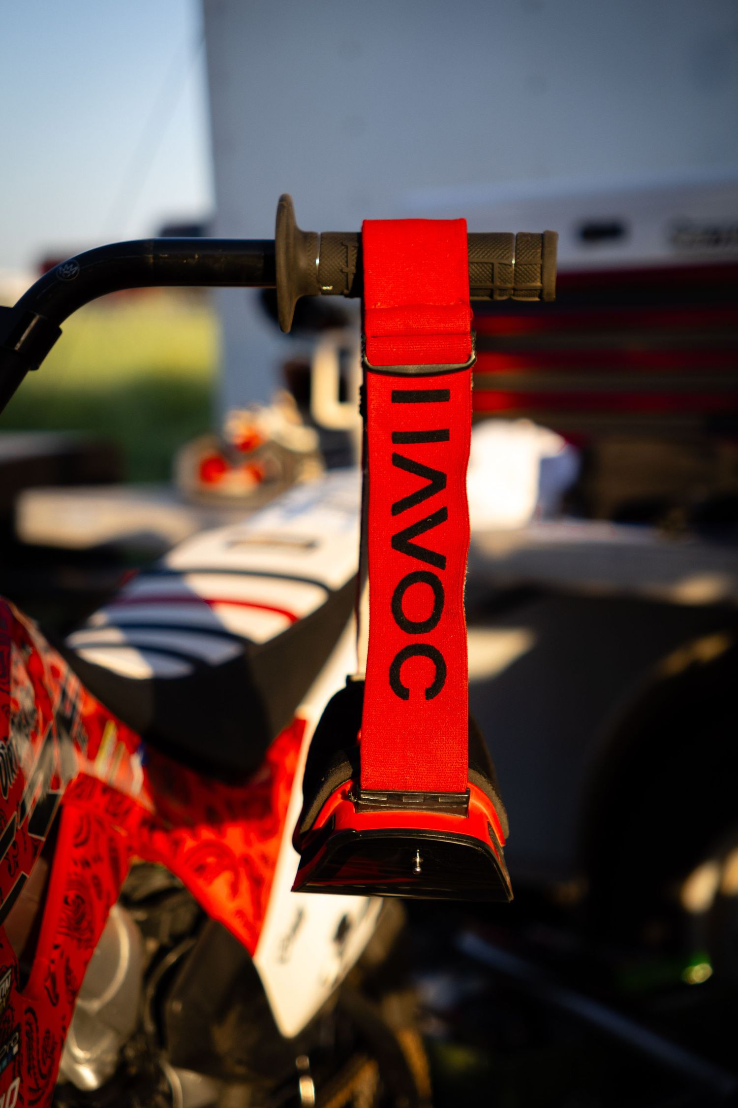Red AVOC branded handlebar strap on a motocross bike handgrip in golden hour light.