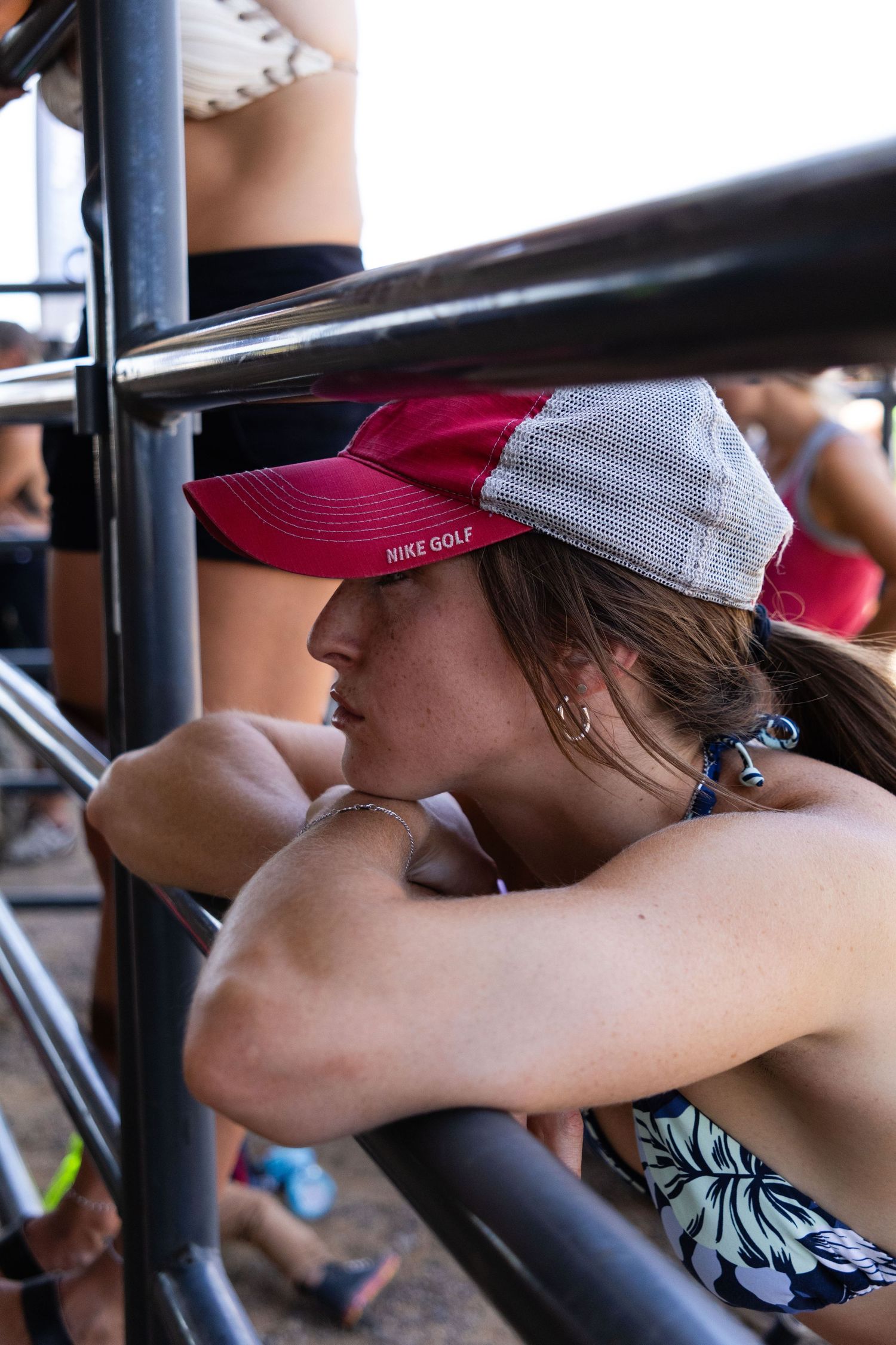 Young woman in a pink Nike Golf cap resting her arms on metal railings at a motocross event.