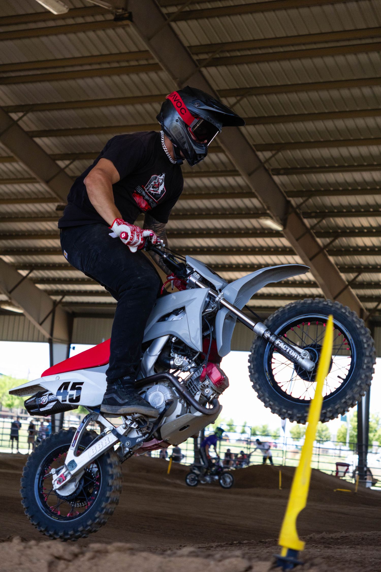 Motocross rider on number 45 dirt bike performs a wheelie jump inside a covered supercross venue.