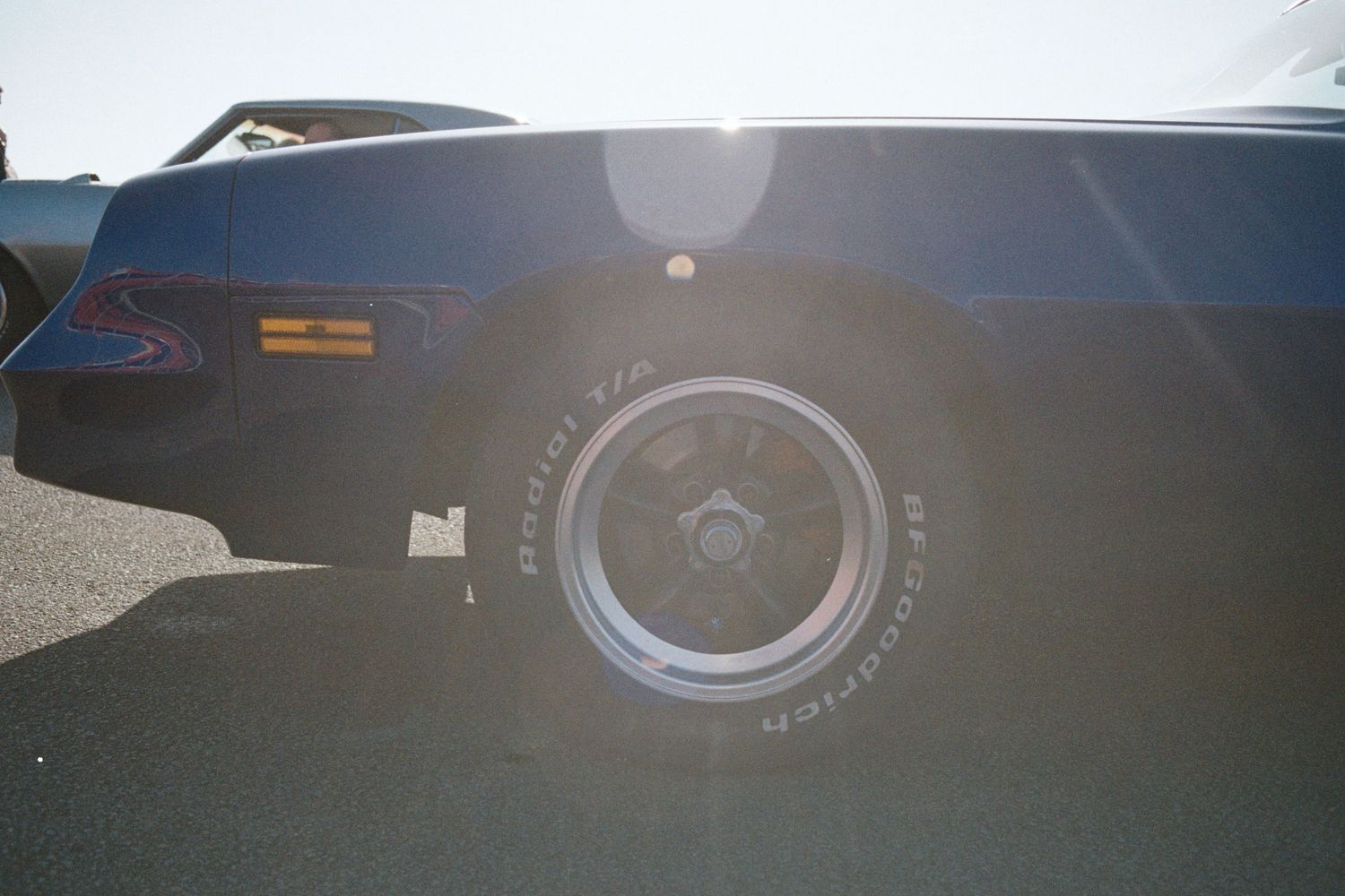Close-up of a classic muscle car wheel with BF Goodrich tire in bright sunlight on pavement.