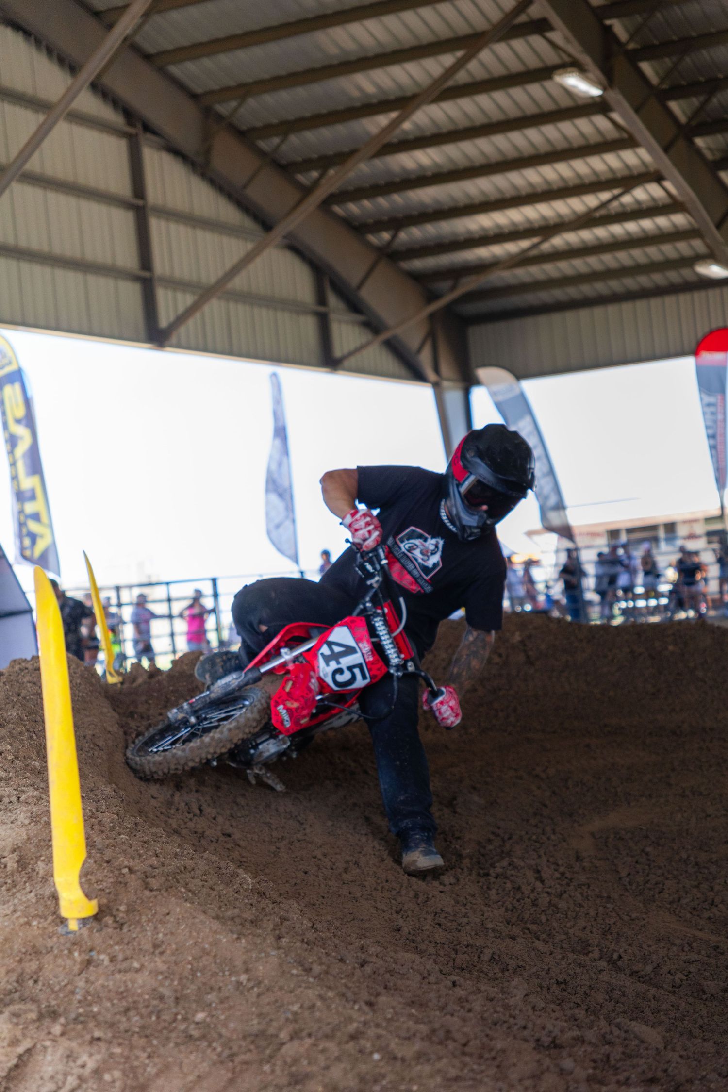 Rider number 45 corners sharply on a red dirt bike on an indoor motocross track.