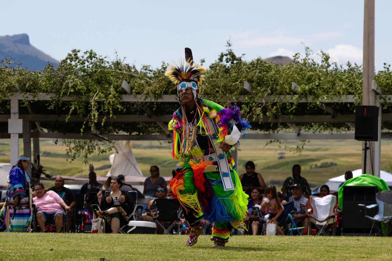 Native American fancy dancer in vibrant multicolored regalia performing before crowd at powwow.