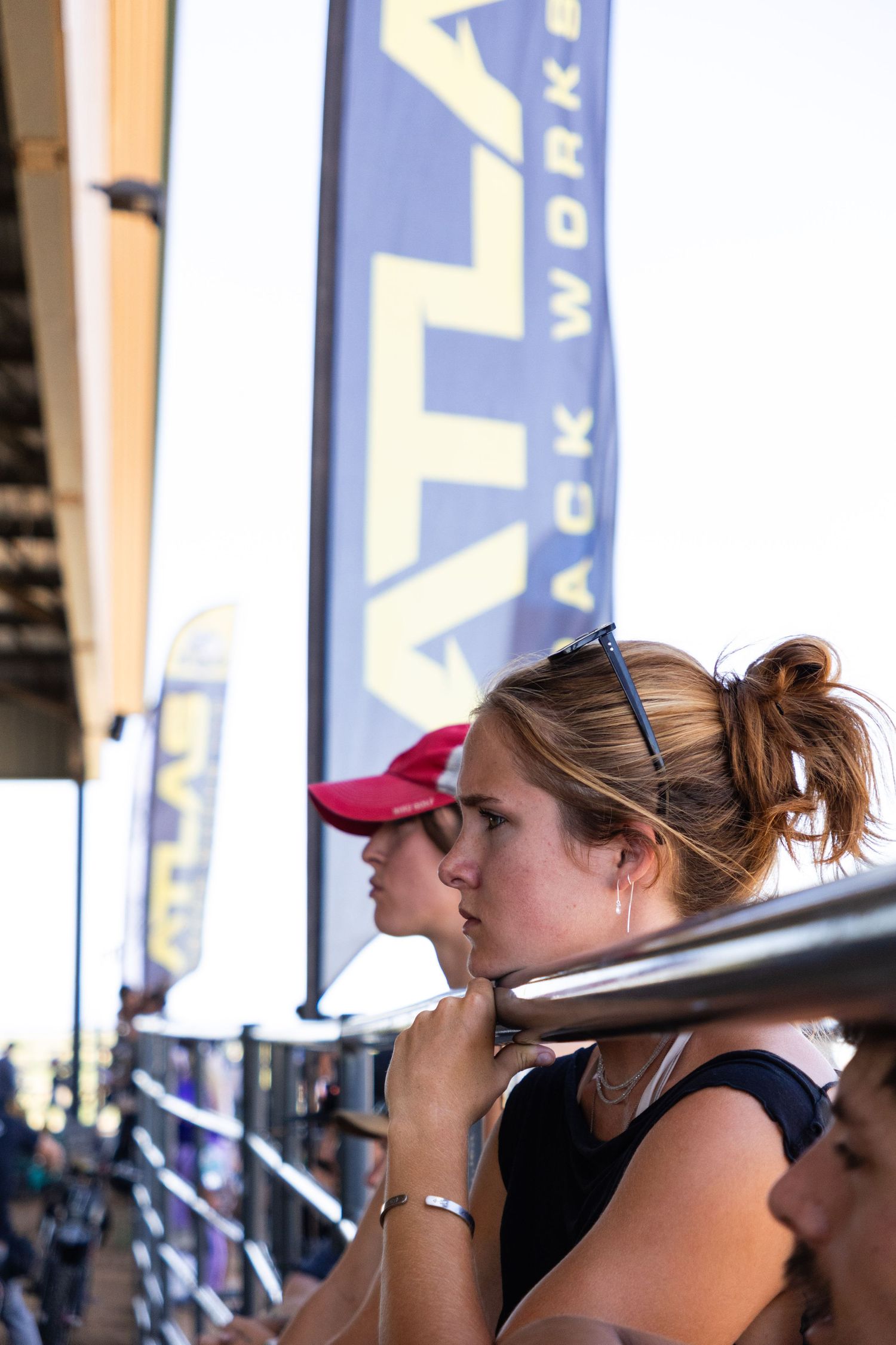 Female spectator with blonde hair watching a motorsport event near Atlas Rack Works banners.