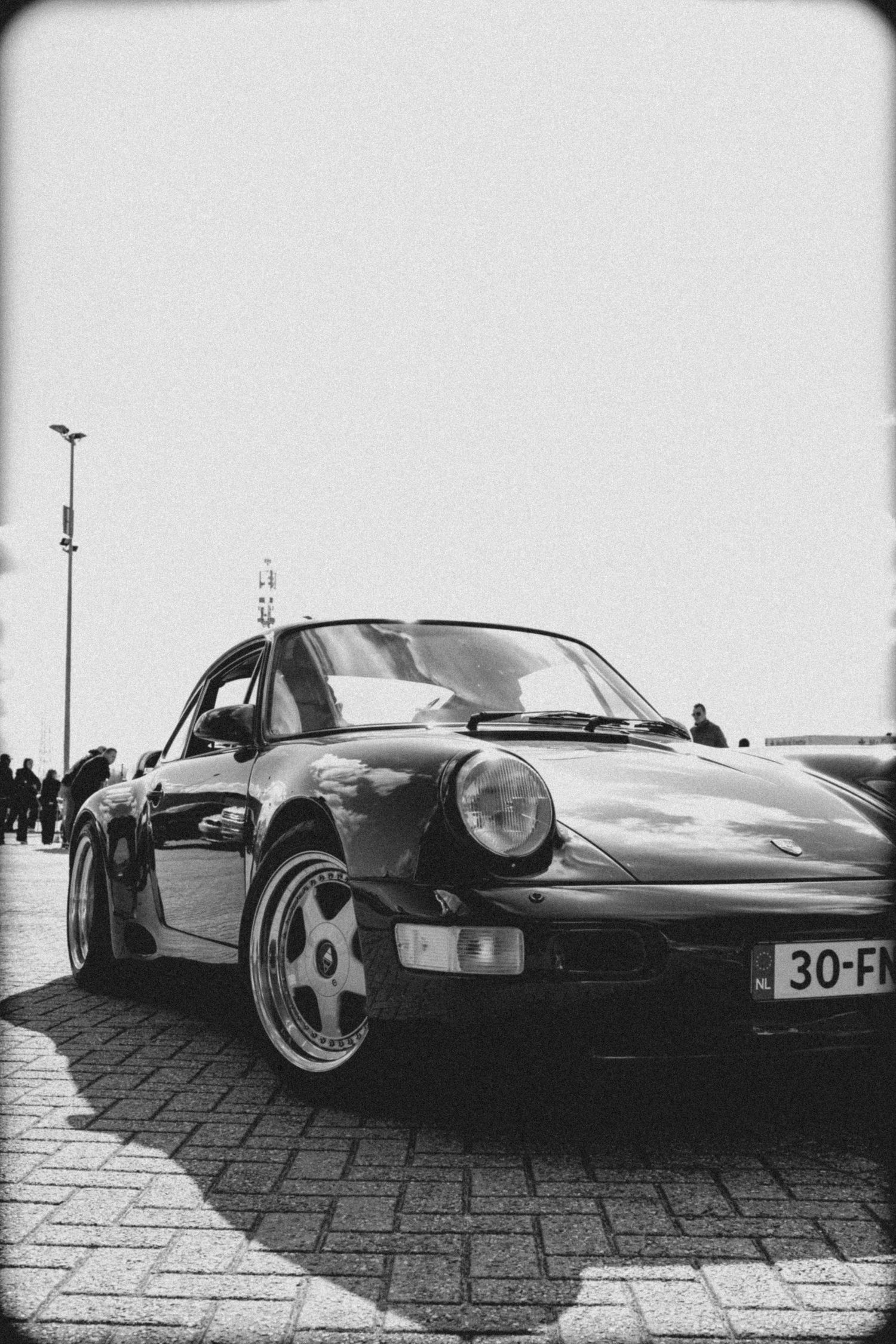Black and white photo of a classic Porsche 911 with license plate 30-FM parked on cobblestone street.