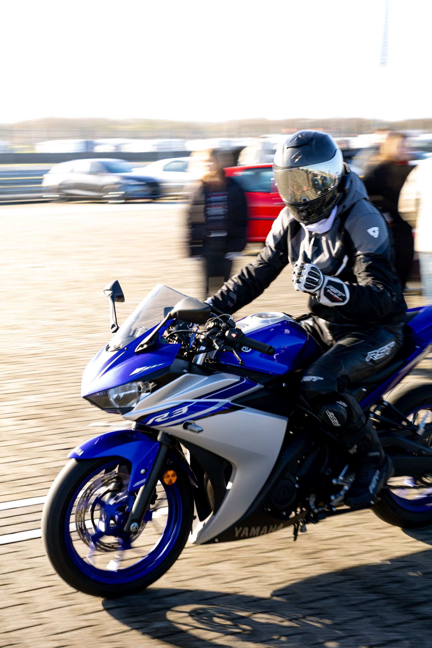 A motorcyclist in black leather jacket and helmet rides a blue Yamaha sport bike on a paved track.