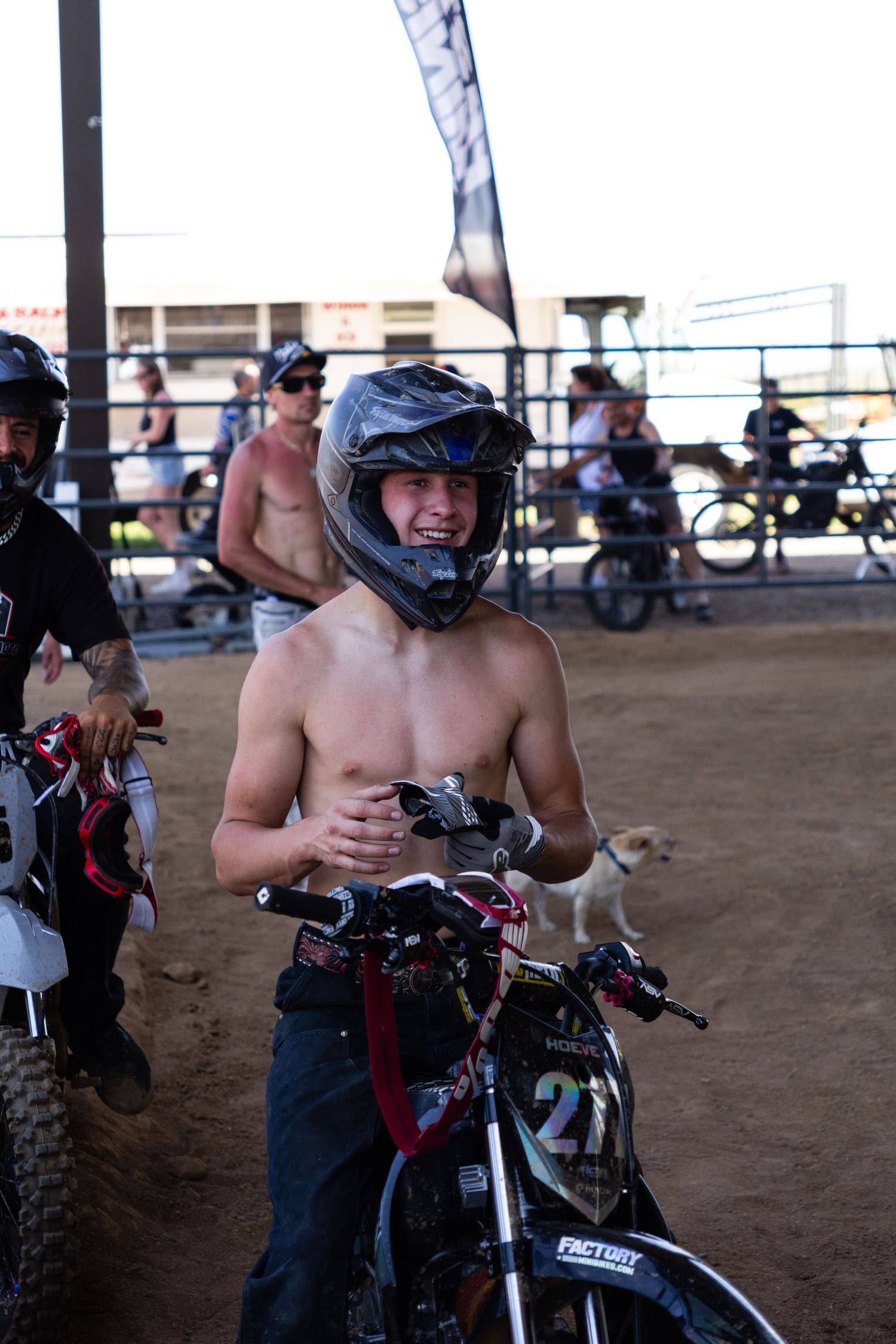 Shirtless motocross rider wearing helmet holds bike #21 at an outdoor dirt arena competition.