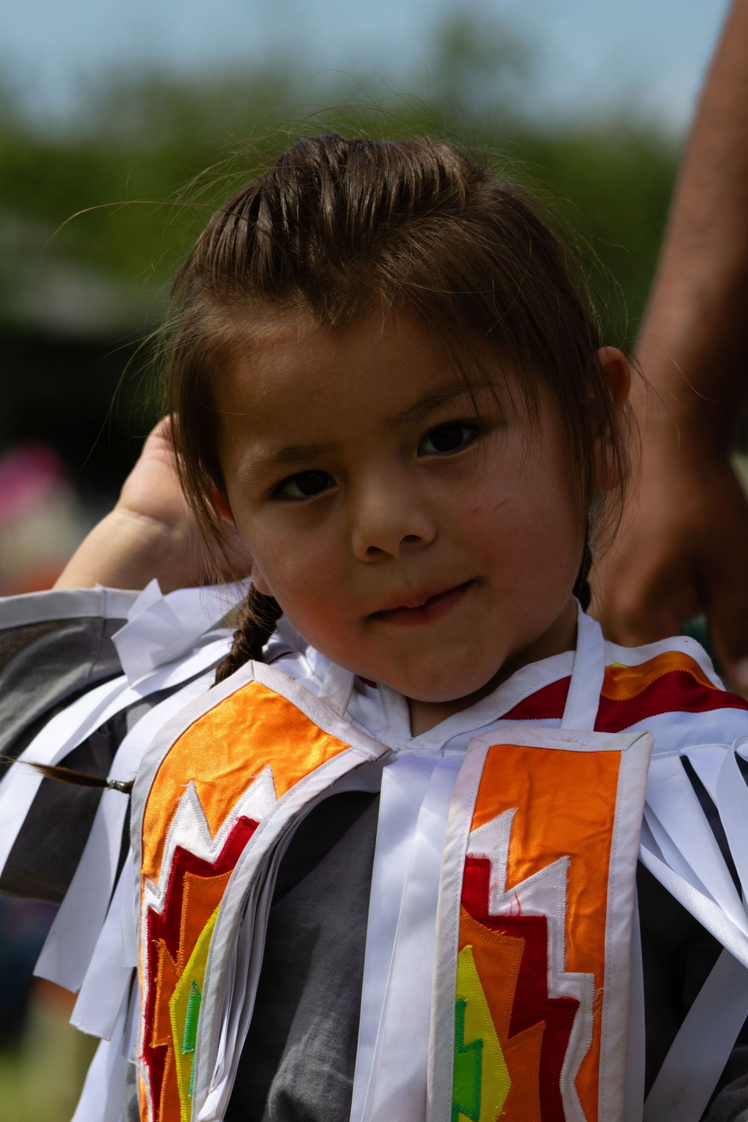 Young Native American child in traditional white and orange regalia at a powwow.