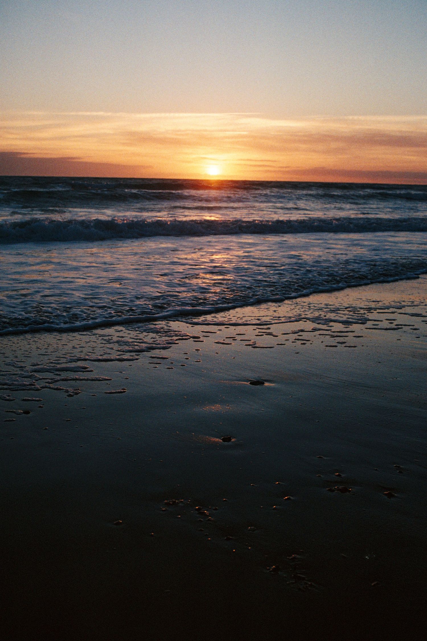 Golden sunset over ocean waves gently washing onto dark sandy beach with colorful sky reflections in Cadiz Spain