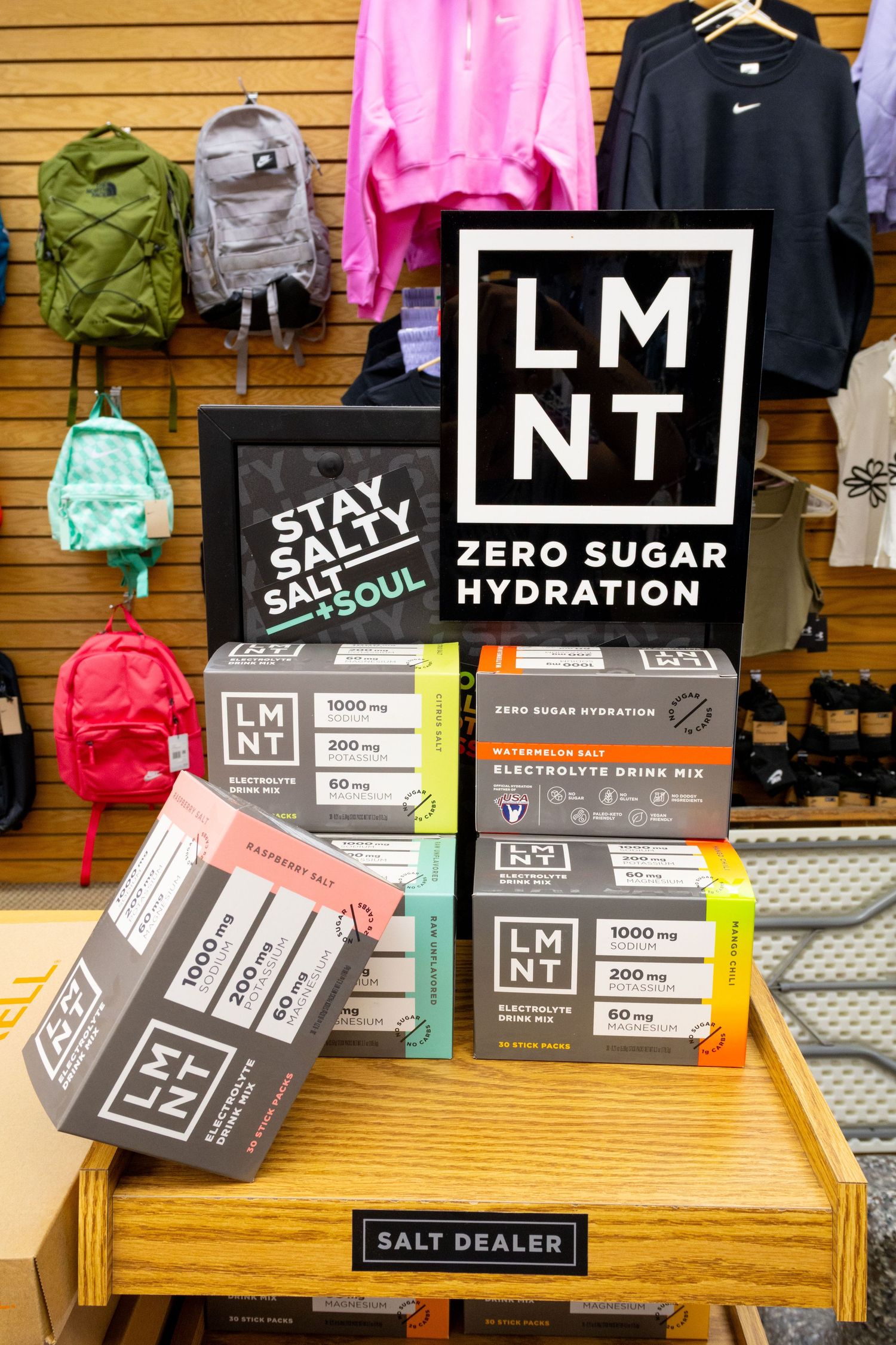LMNT zero sugar hydration electrolyte drink mix products displayed on a wooden shelf in a retail store.