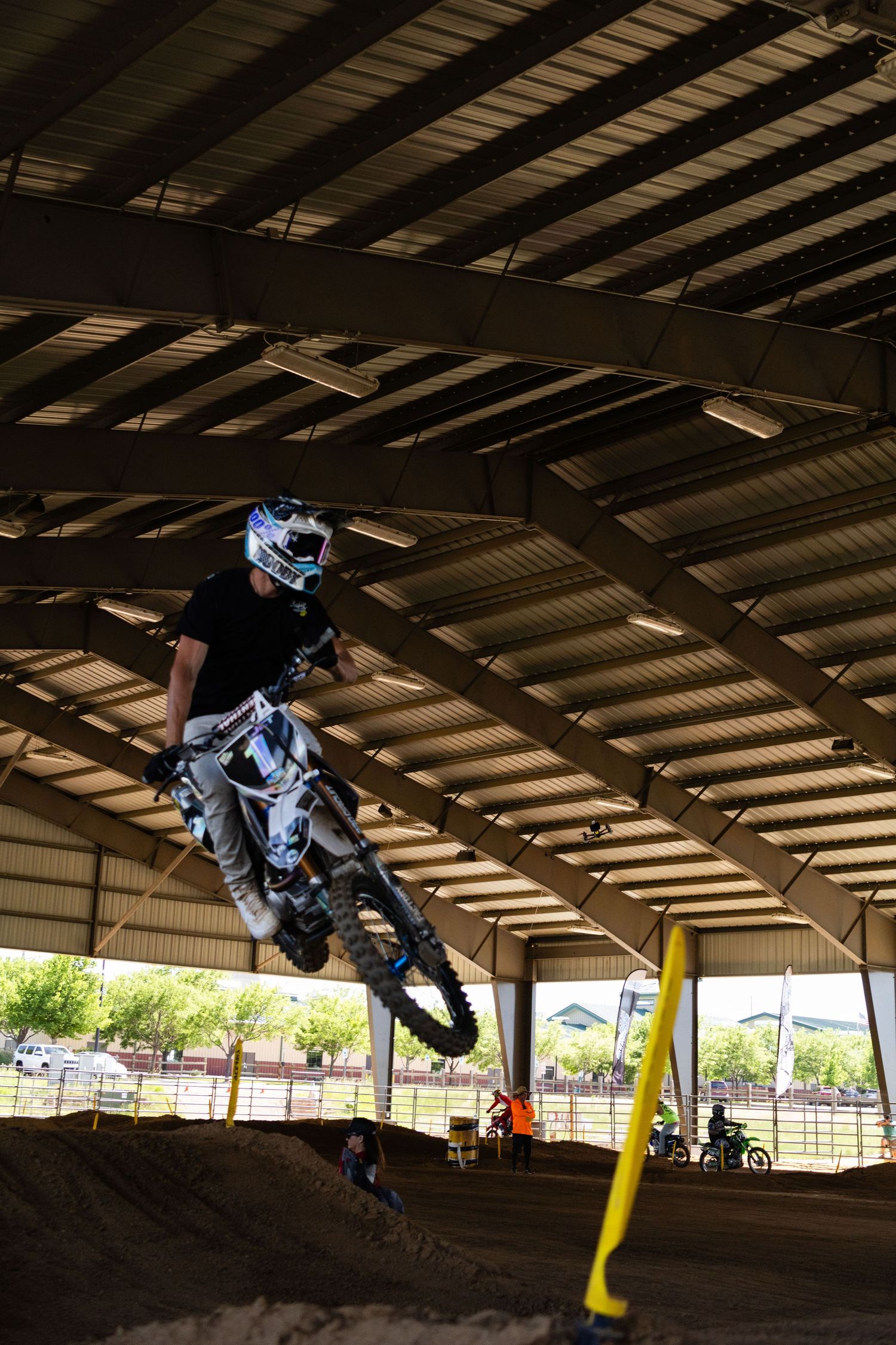 Motocross rider in white helmet catches big air over dirt jump at indoor supercross track.