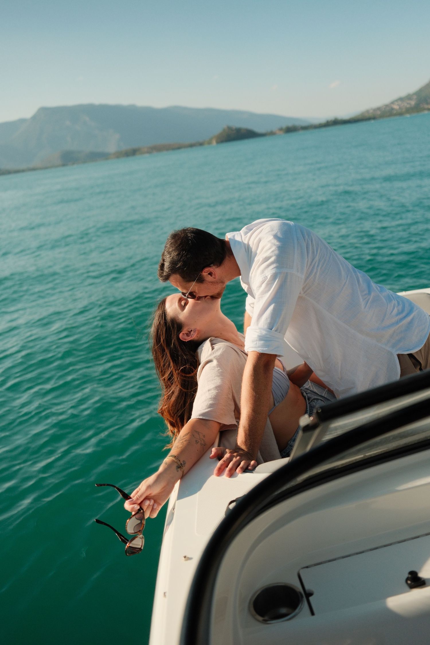 Romantic couple kissing on a luxury boat with turquoise water and mountains in the background.