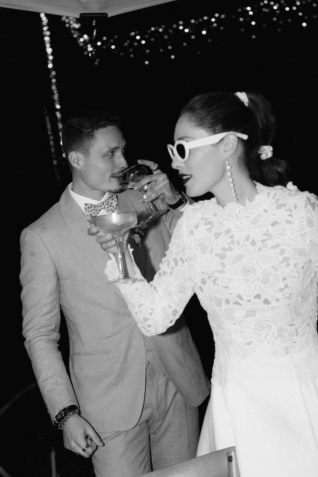 Black and white photo of bride in sunglasses and groom toasting with champagne glasses at wedding reception.