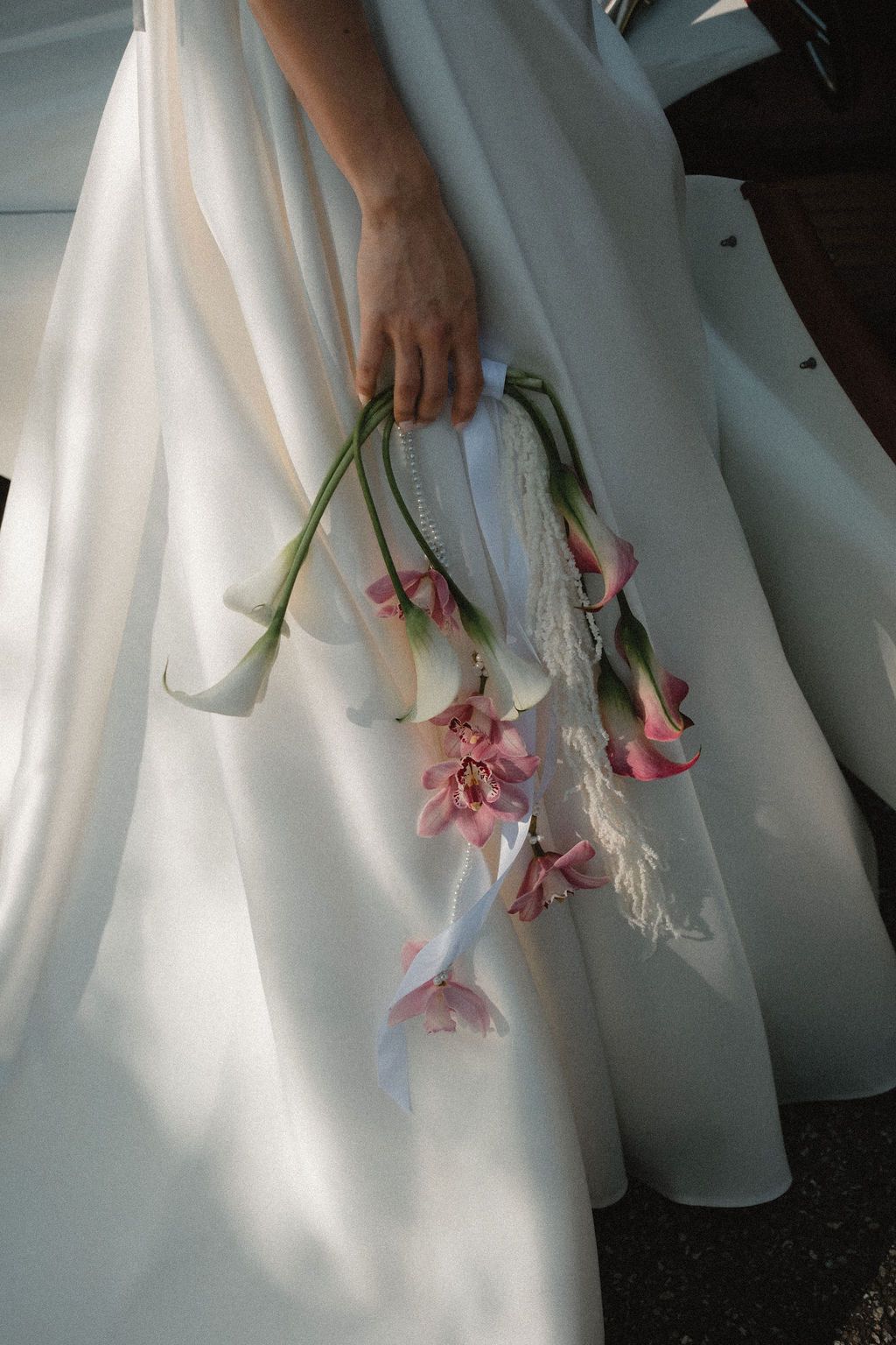 Bride holds elegant cascading bouquet of pink and white calla lilies against flowing white wedding gown.