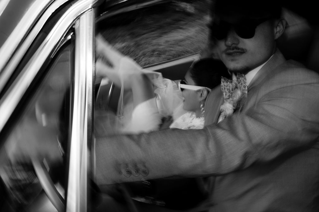 Black and white candid photo of bride and groom sharing intimate moment inside vintage classic car.