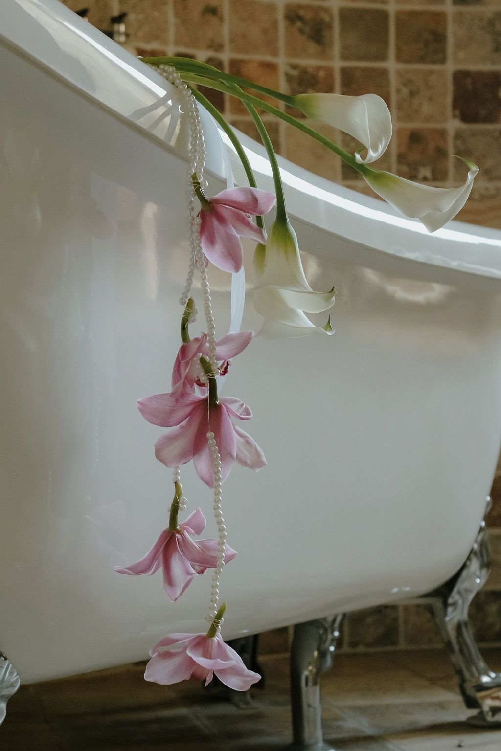 Pink flowers and pearls draped over a white clawfoot bathtub in an elegant bathroom.