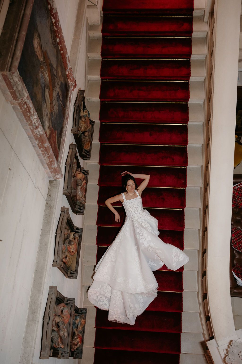 Bride in white gown lying on red carpeted staircase in ornate historic building.