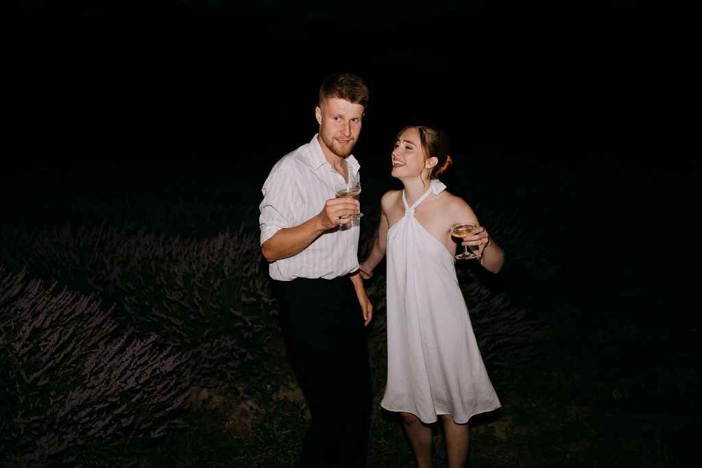 Couple sharing a romantic moment at night in a lavender field, holding champagne glasses.