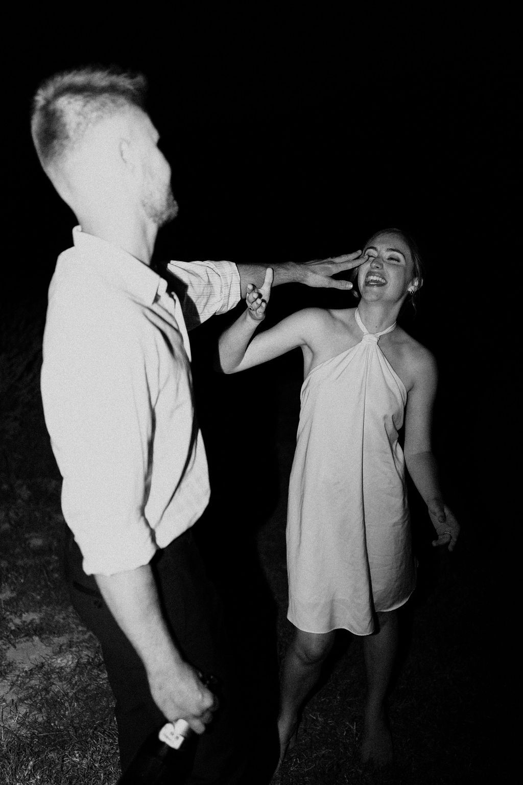 Black and white candid photo of couple laughing and dancing together outdoors at night wedding reception.