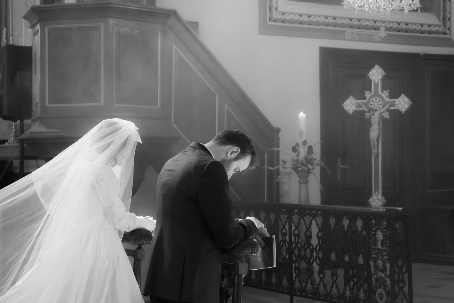 Black and white photo of a bride and groom bowing in prayer at a church altar during their wedding ceremony.