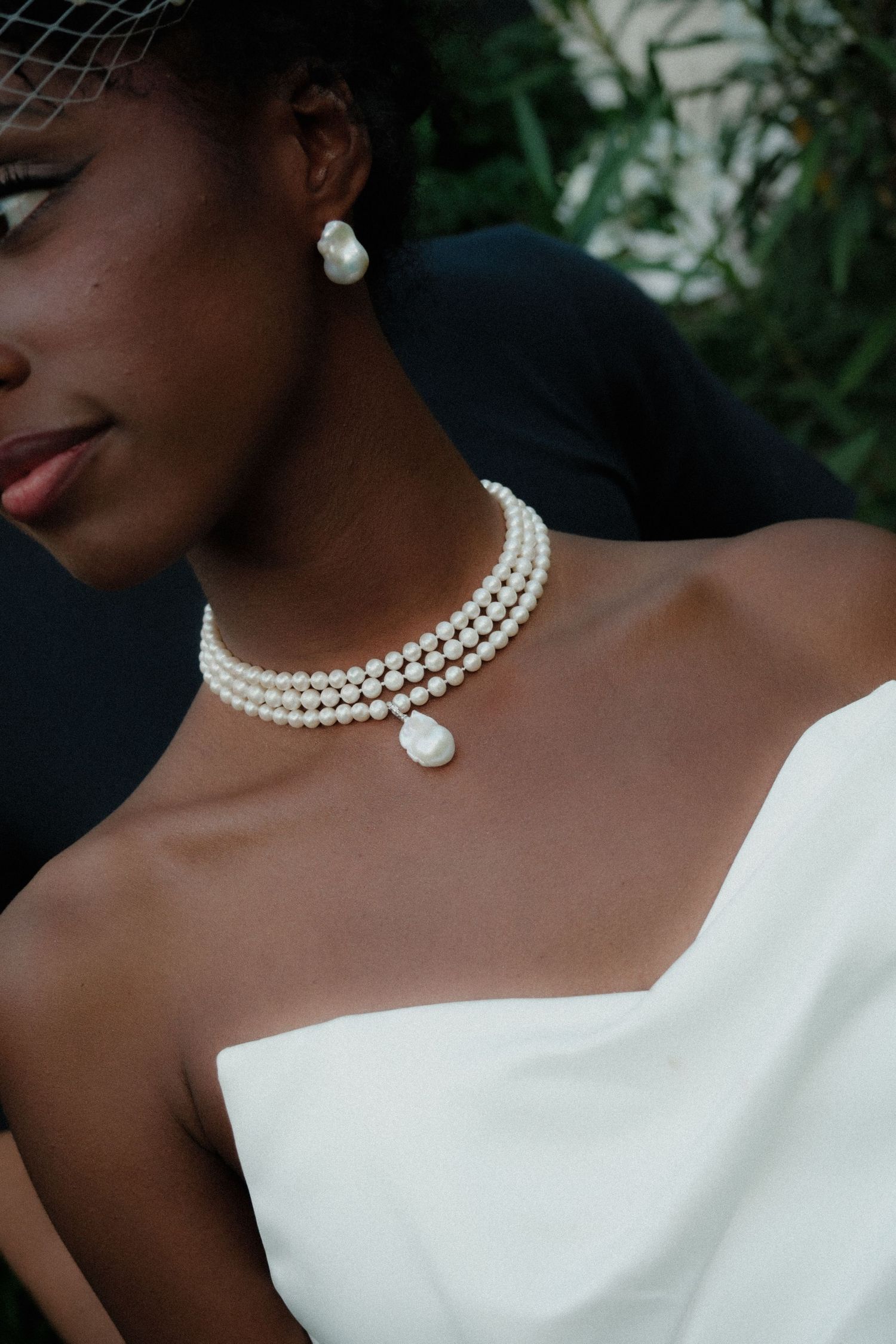 Bride wearing elegant triple-strand pearl choker necklace with baroque pearl drop and matching earrings with white strapless gown.