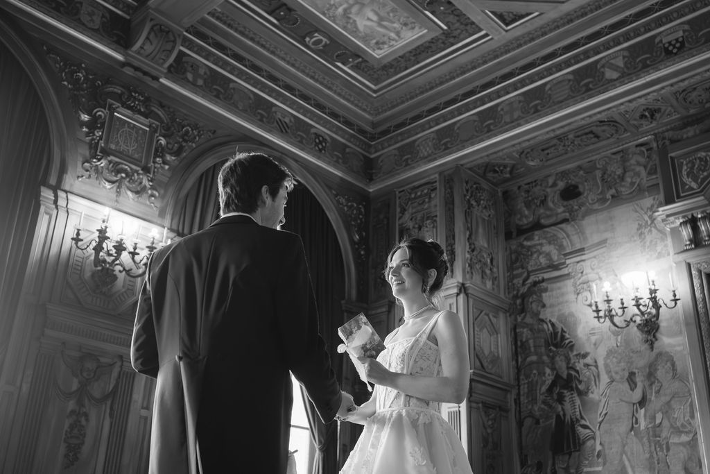 Bride and groom exchange vows in an ornate baroque ballroom with frescoed ceilings in black and white.