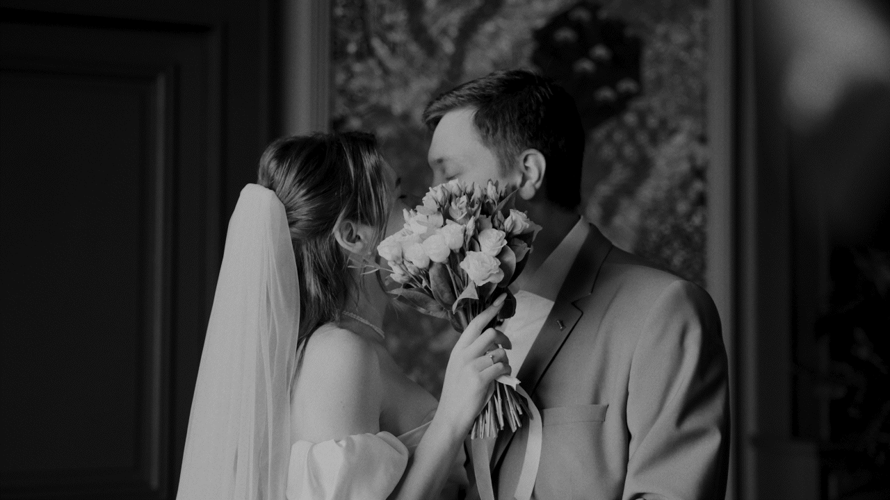 Black and white couple of bride and groom kissing hiding by a bouquet