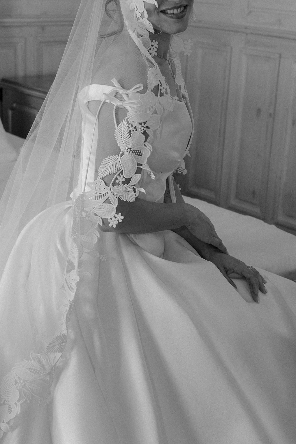 Black and white close-up of bride in satin gown with lace-trimmed veil and ribbon details.