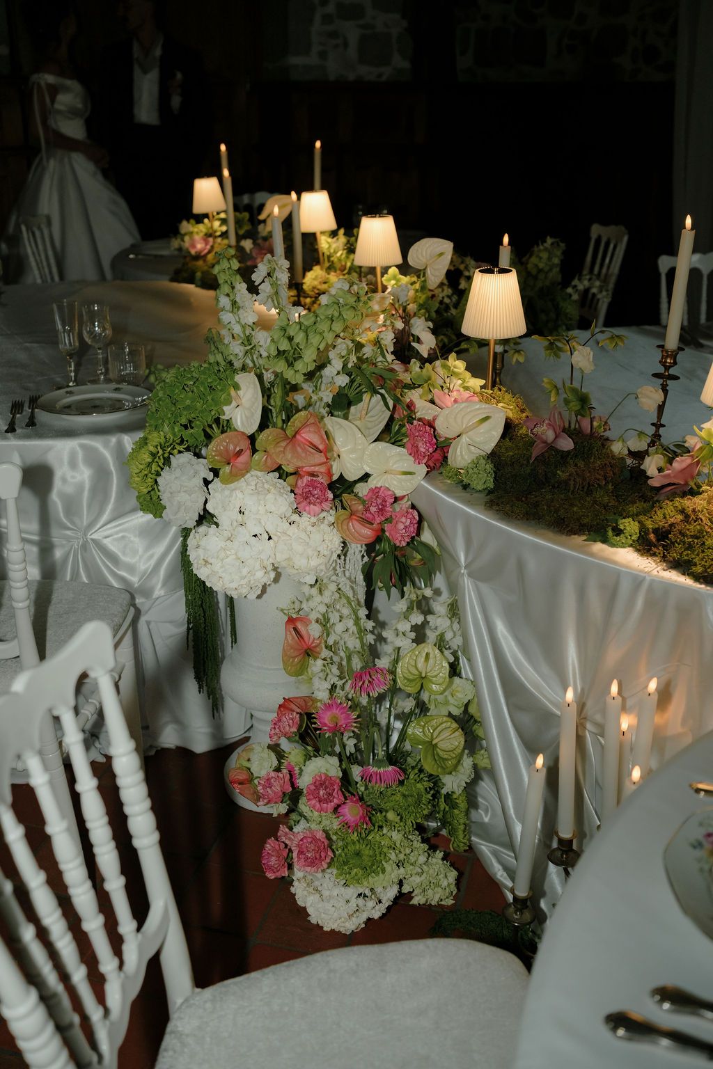 Lush floral centerpiece with pink roses and white flowers adorning candlelit wedding reception table.