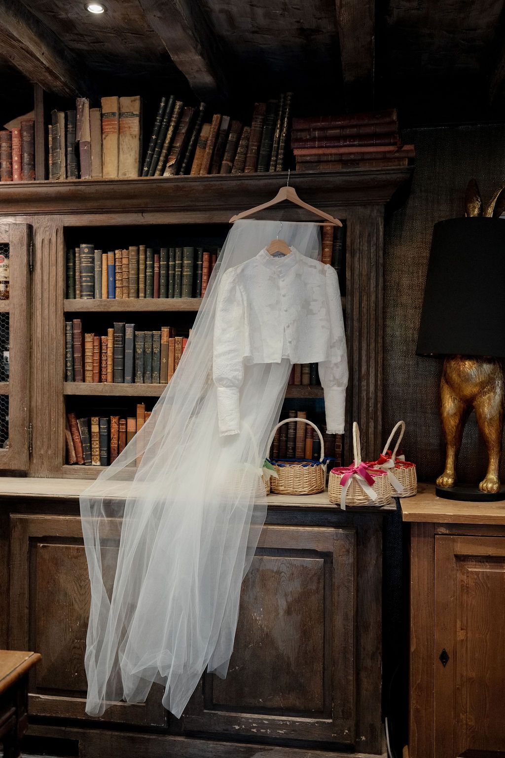 White wedding jacket and veil hanging on a hanger in a rustic library with vintage books.