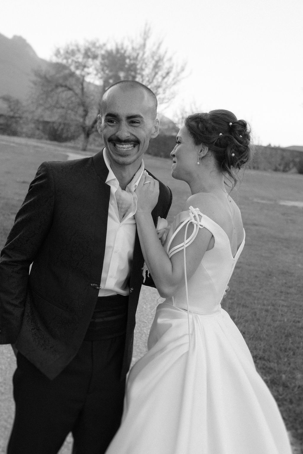Black and white romantic photo of a bride and groom kissing while holding a floral bouquet indoors.
