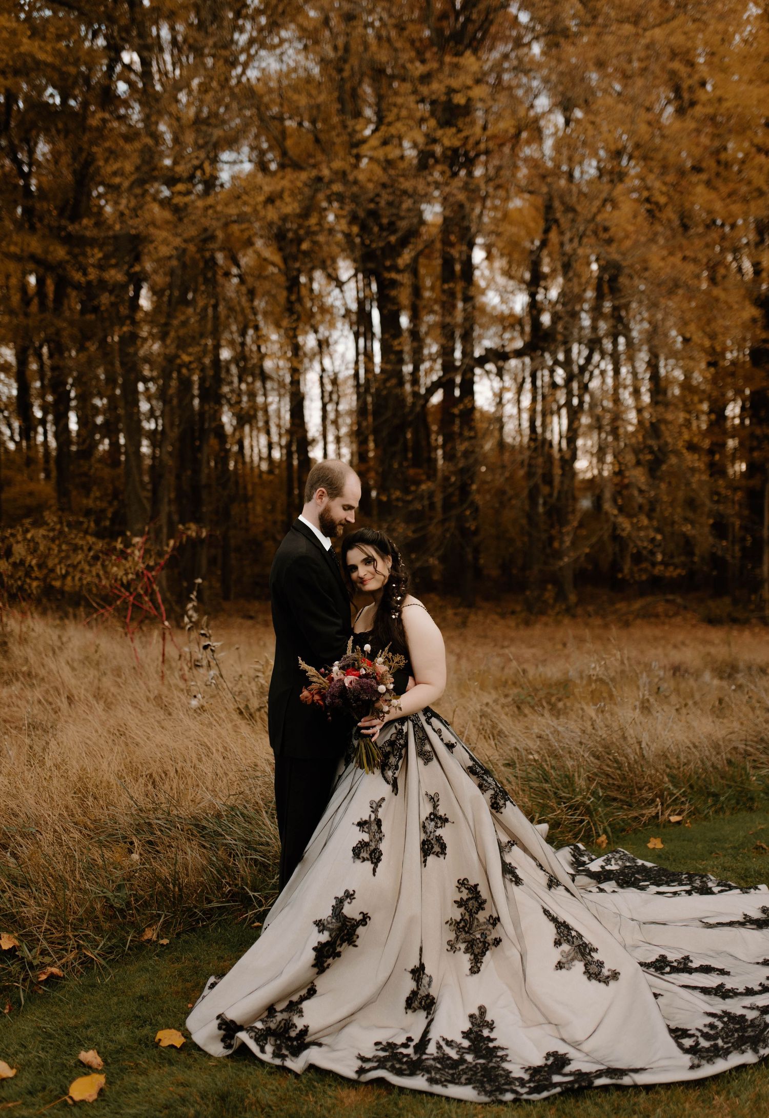 A couple poses in autumn foliage with a dramatic black and white wedding gown.
