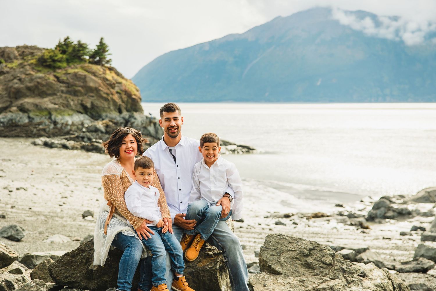 Family enjoying time together on rocky beach with mountains and ocean views.