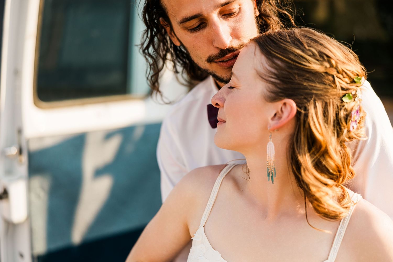 A couple shares an intimate moment together in warm sunlight next to a vintage vehicle.